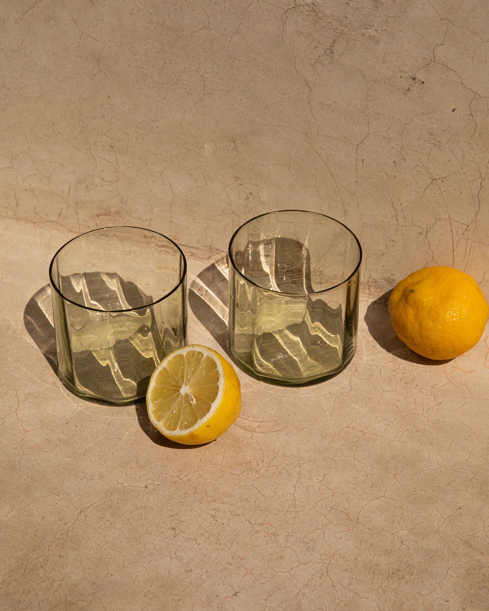 Zwei leere Gläser auf einem Tisch neben einer ganzen und einer halben Zitrone.