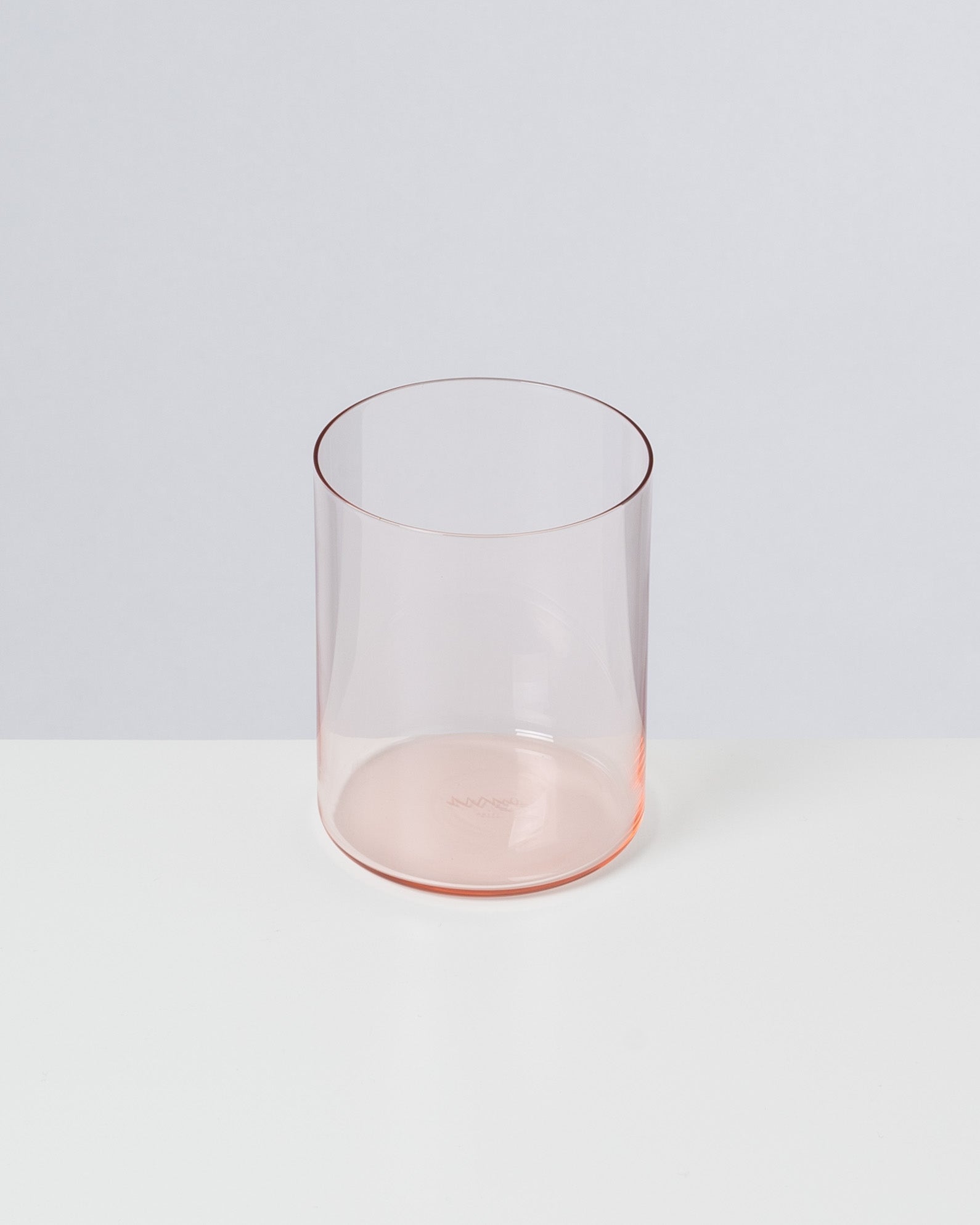 Ein rosa, transparentes Glas steht auf einer weißen Oberfläche vor einem grauen Hintergrund.