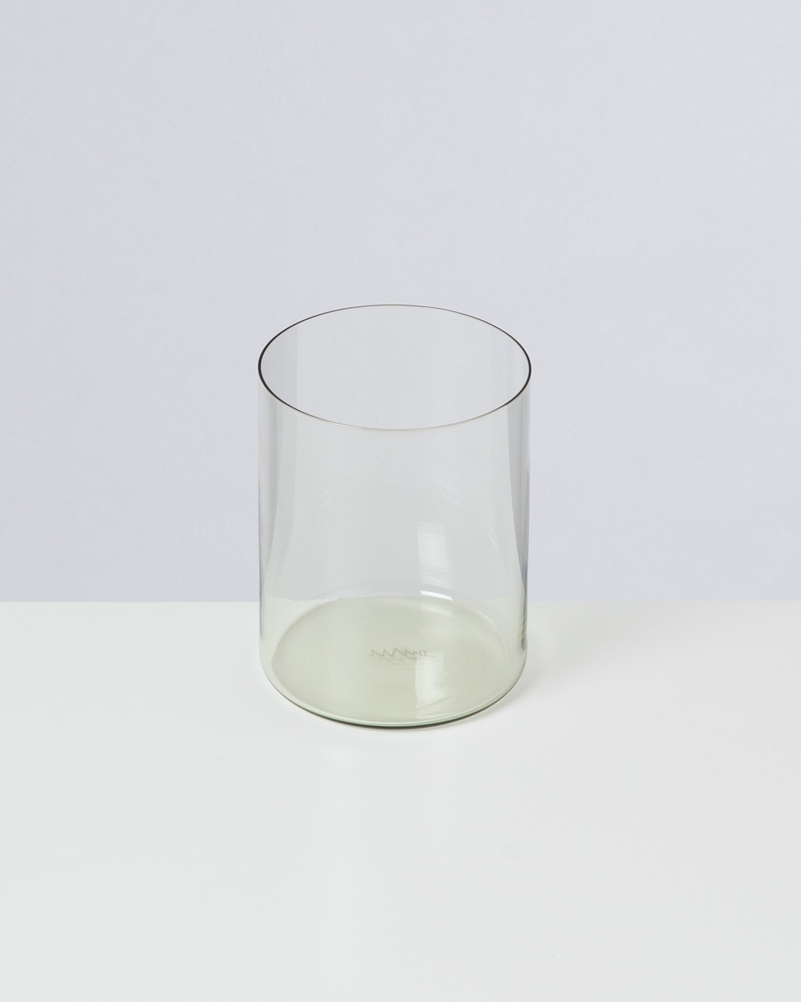 Ein transparentes, zylindrisches Glas steht auf einer weißen Oberfläche vor einem hellgrauen Hintergrund.