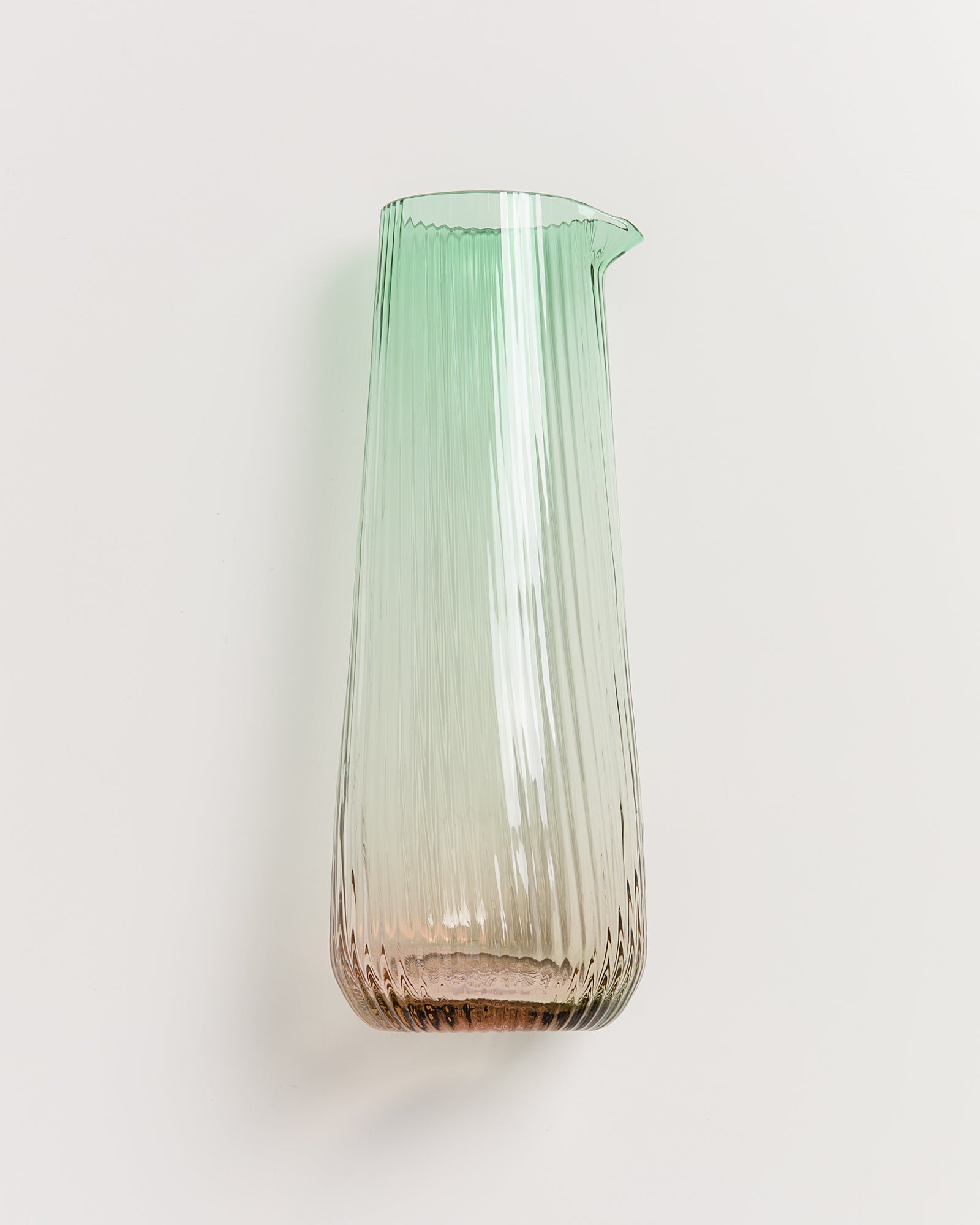 Eine hohe, gestreifte Glaskaraffe mit grünem Farbverlauf steht aufrecht auf einer hellen Oberfläche.