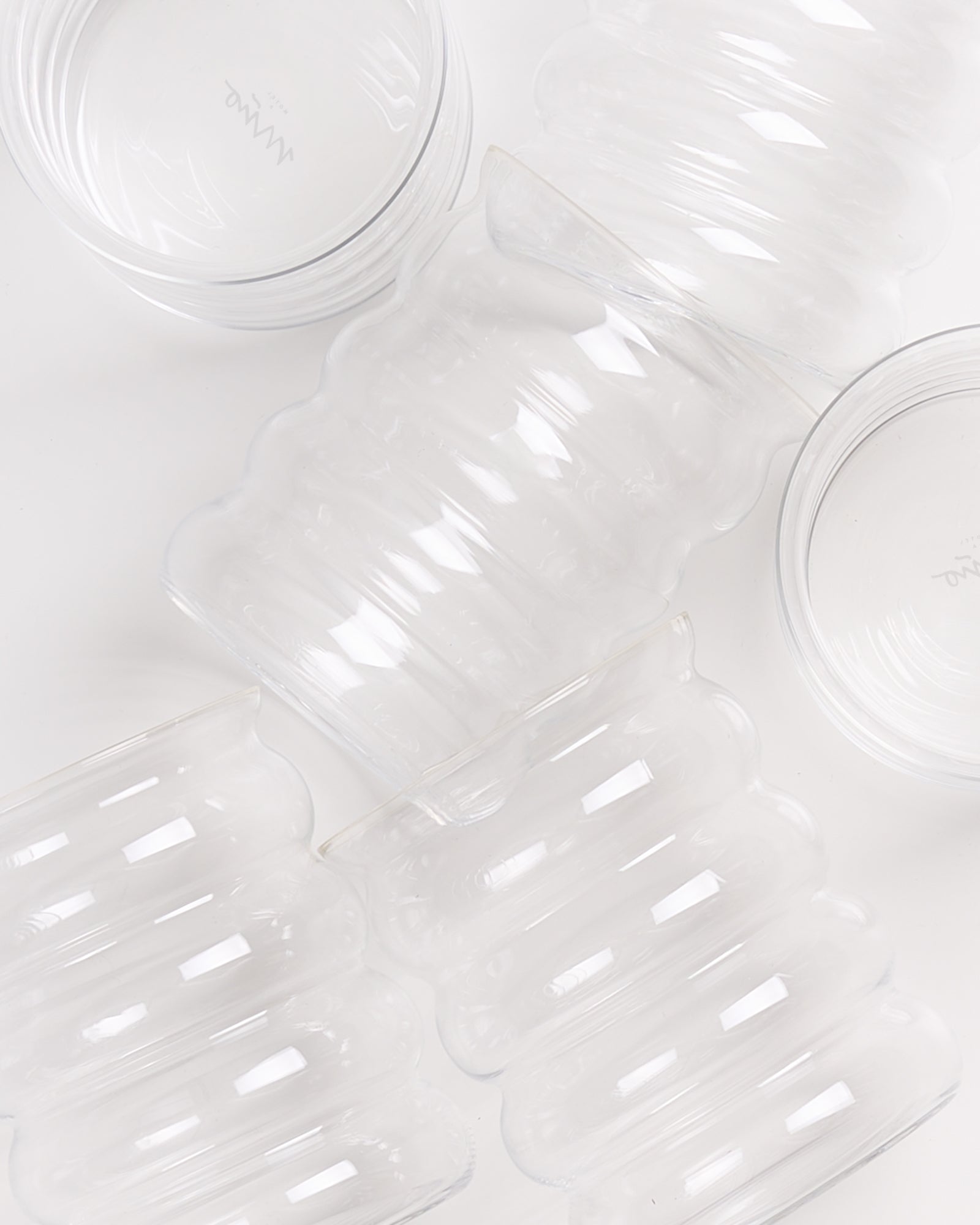 Mehrere durchsichtige Glasgefäße mit wellenförmigem Design auf einer weißen Oberfläche.