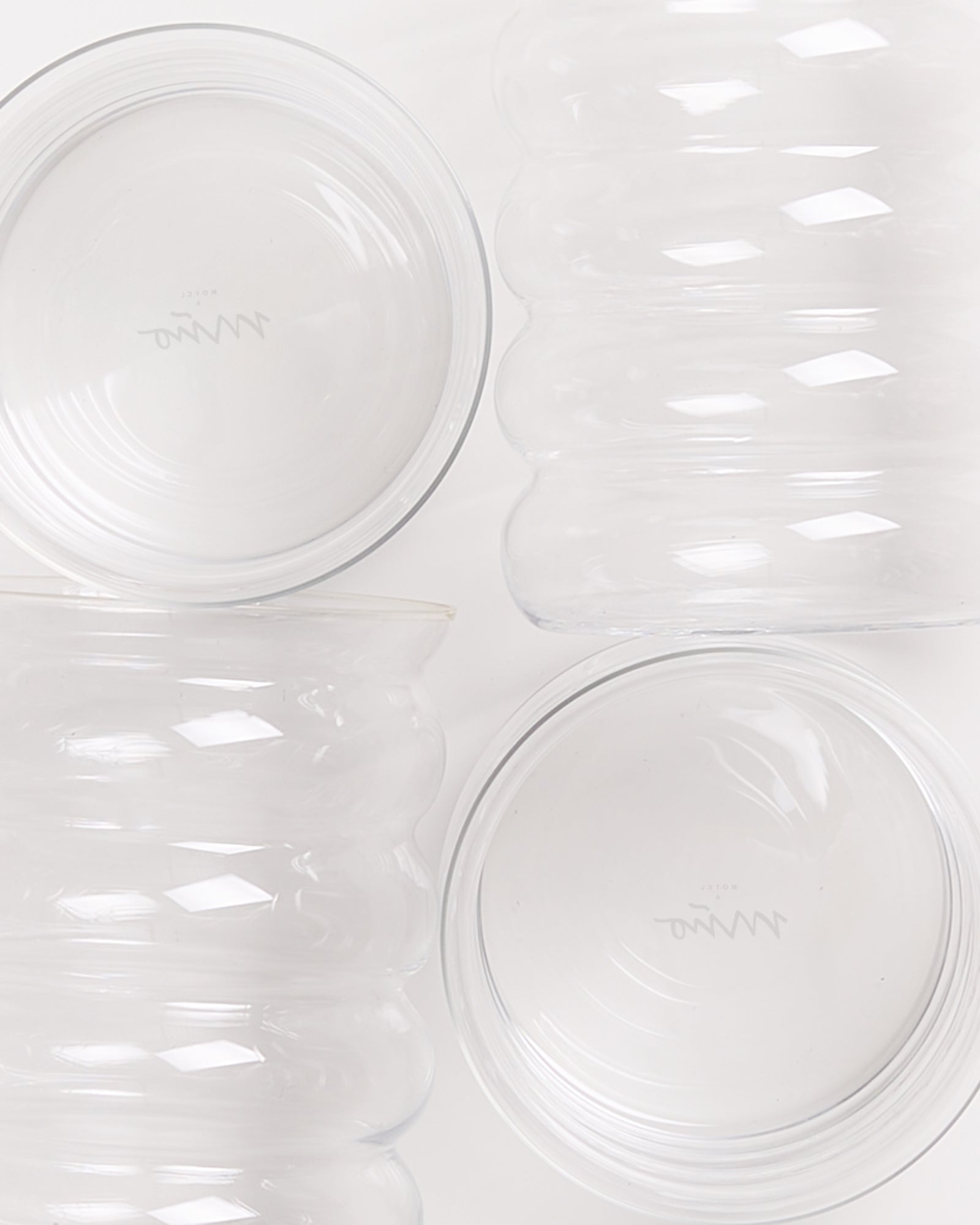 Vier gewellte, durchsichtige Glasschalen auf einer weißen Oberfläche.