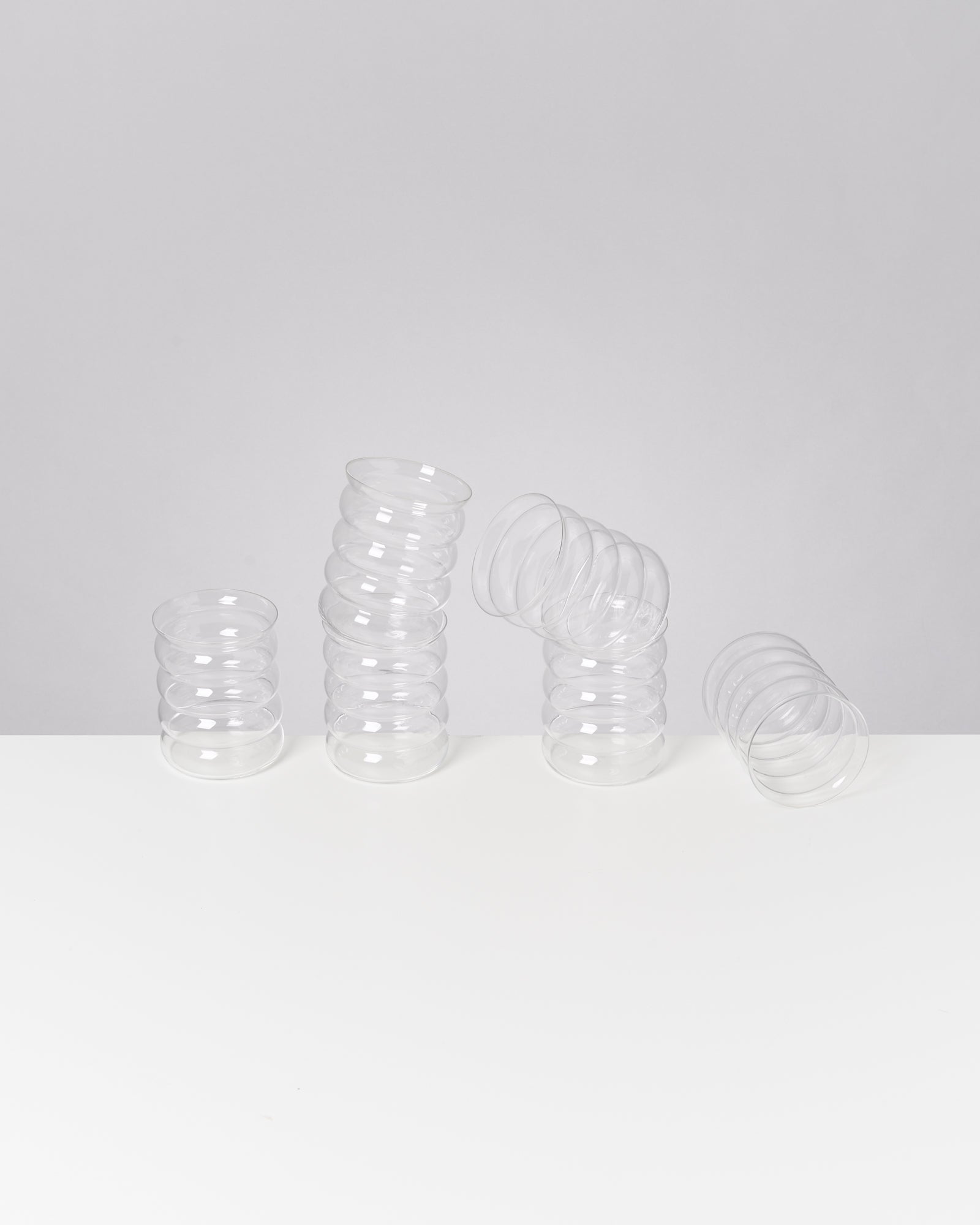 Drei ineinander gestapelte, durchsichtige Plastikbecher liegen auf einem weißen Tisch vor einem grauen Hintergrund.