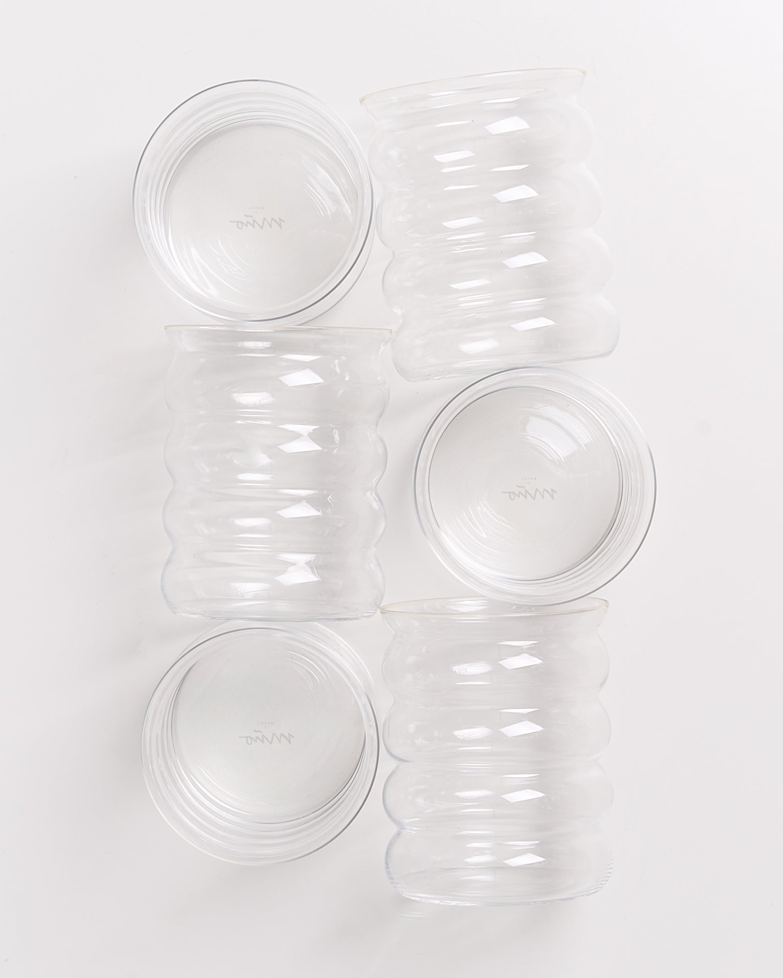 Fünf gewellte Glasgefäße stehen aufrecht und seitlich auf einem weißen Hintergrund.