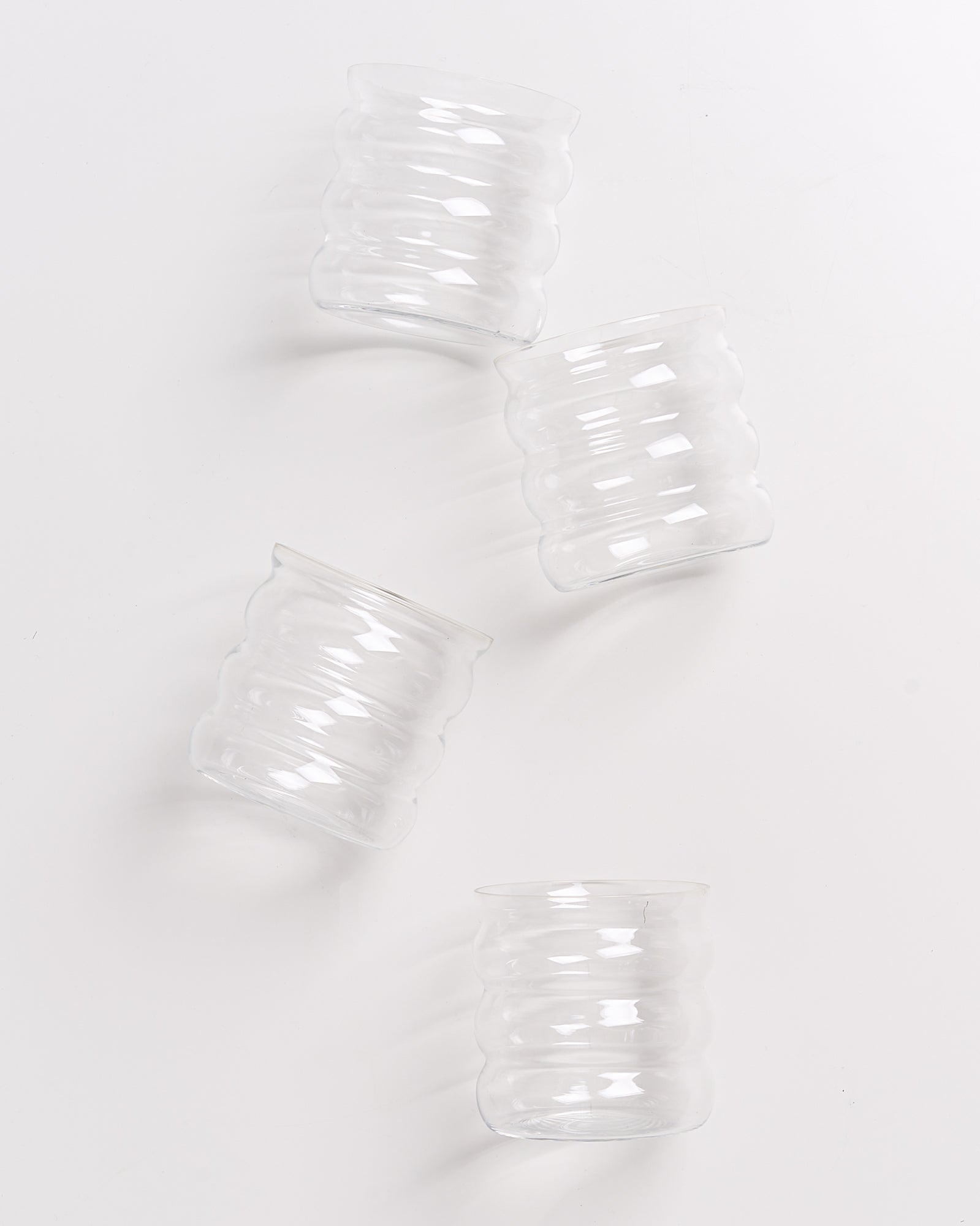 Vier transparente, gewellte Trinkgläser liegen auf weißem Hintergrund verstreut.
