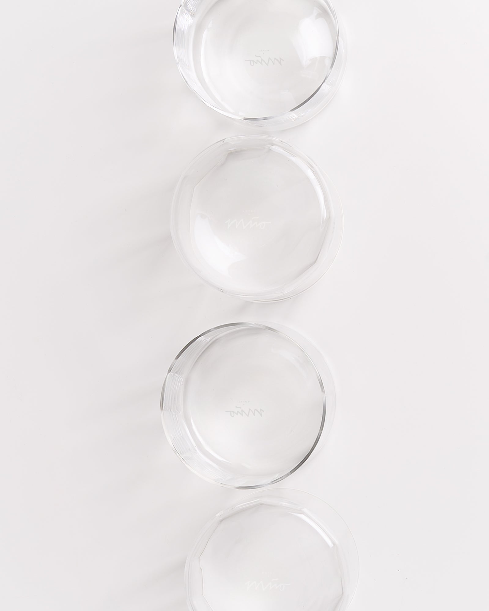 Vier klare Glasschalen sind in einer vertikalen Reihe auf einem weißen Hintergrund angeordnet.