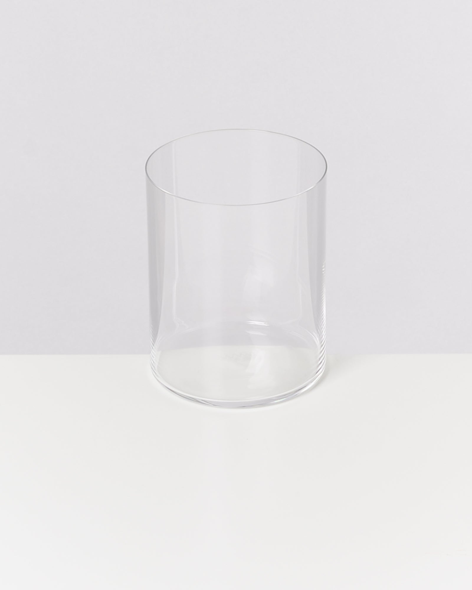 Ein leeres, transparentes Trinkglas steht auf einem weißen Tisch vor einem grauen Hintergrund.