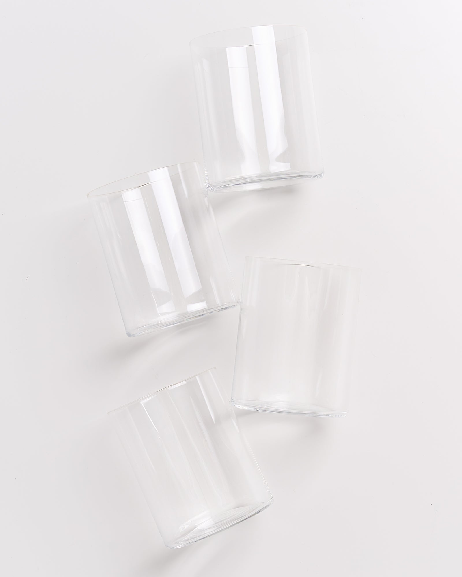 Vier leere Trinkgläser liegen schräg auf einer weißen Oberfläche.