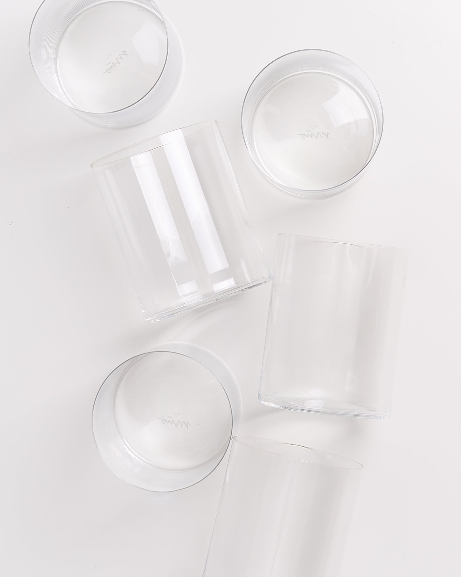 Fünf klare Gläser, teilweise gefüllt mit Wasser, stehen auf einer weißen Oberfläche.