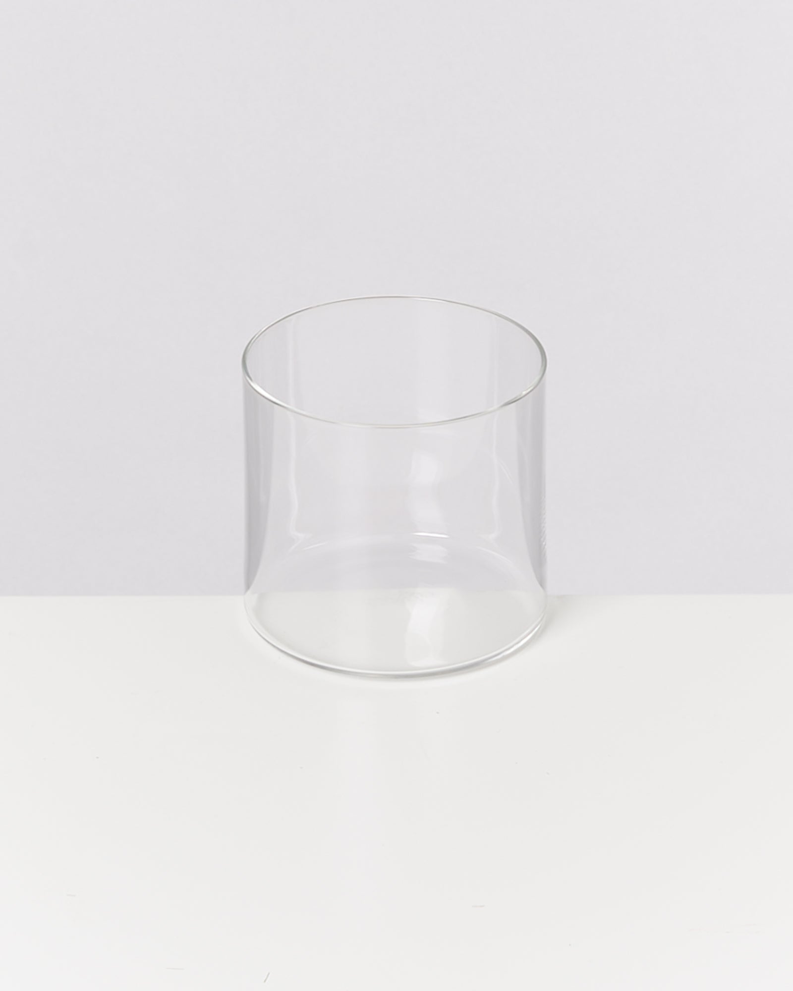 Ein transparentes, leeres Glas steht auf einer weißen Oberfläche vor einem neutralen Hintergrund.