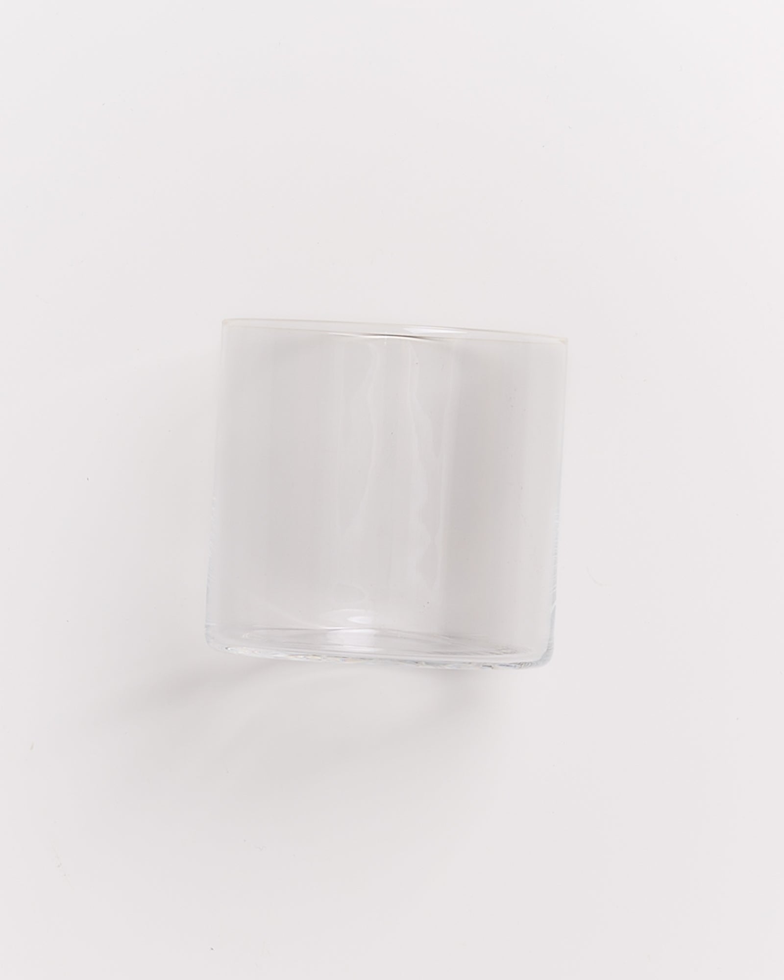 Ein transparentes, leeres Glas steht schräg auf einer weißen Oberfläche.