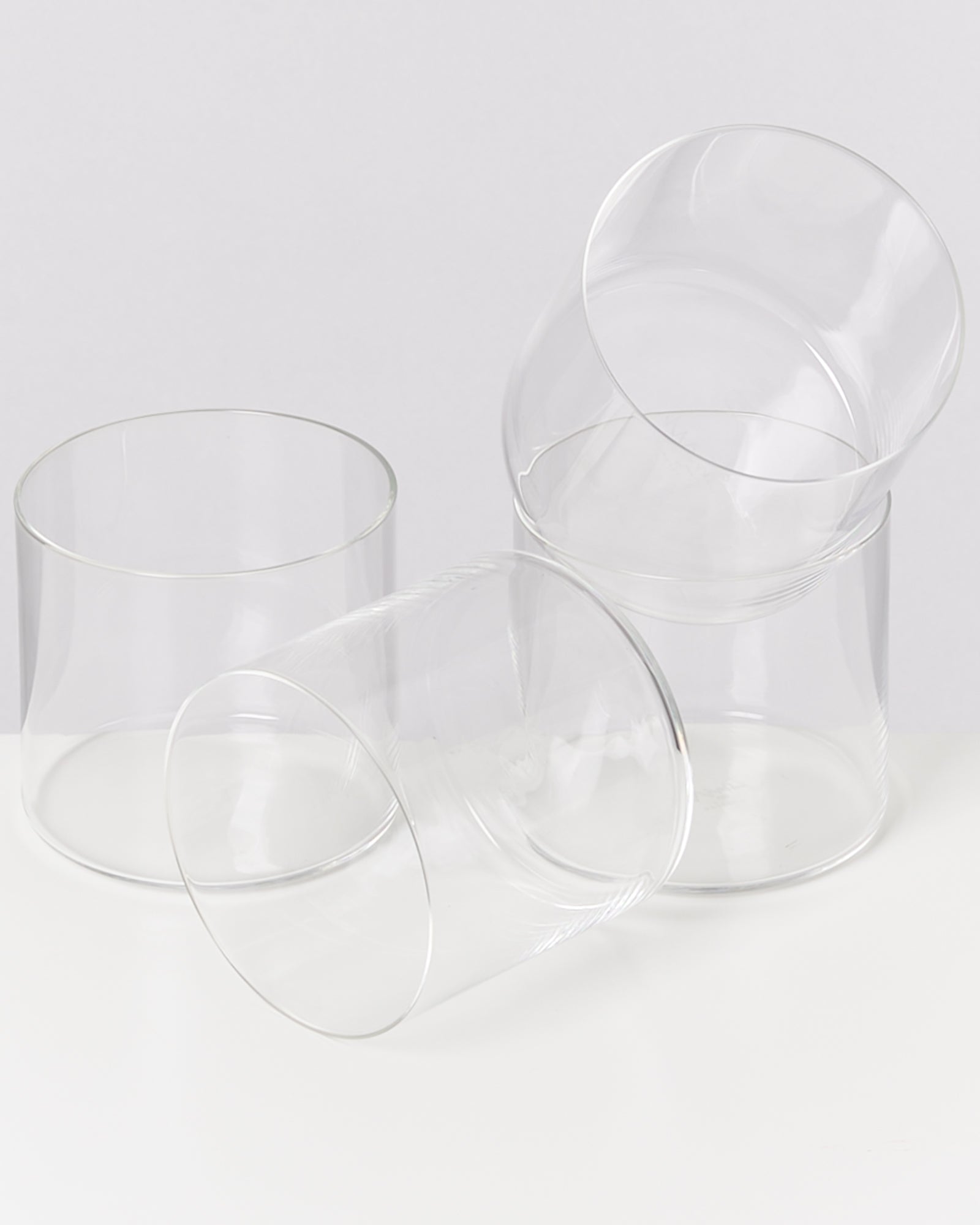 Vier leere, durchsichtige Gläser stehen und liegen auf einem weißen Hintergrund.