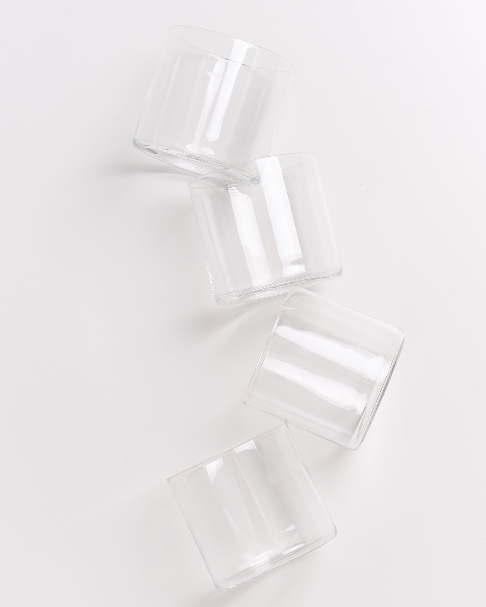 Vier leere, transparente Gläser liegen diagonal auf einer weißen Oberfläche.