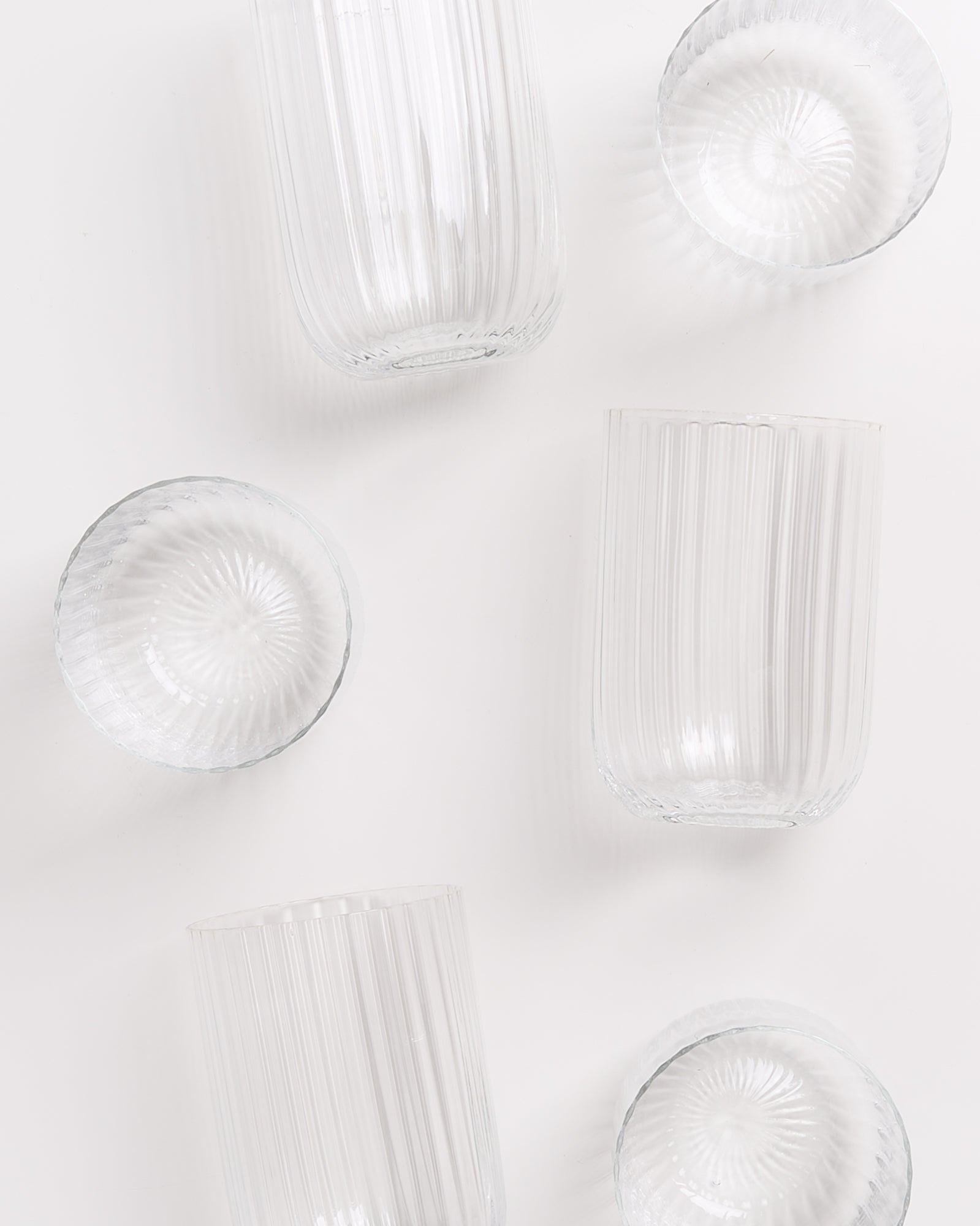 Fünf gerillte, durchsichtige Glasgefäße in verschiedenen Größen liegen auf weißem Hintergrund verteilt.