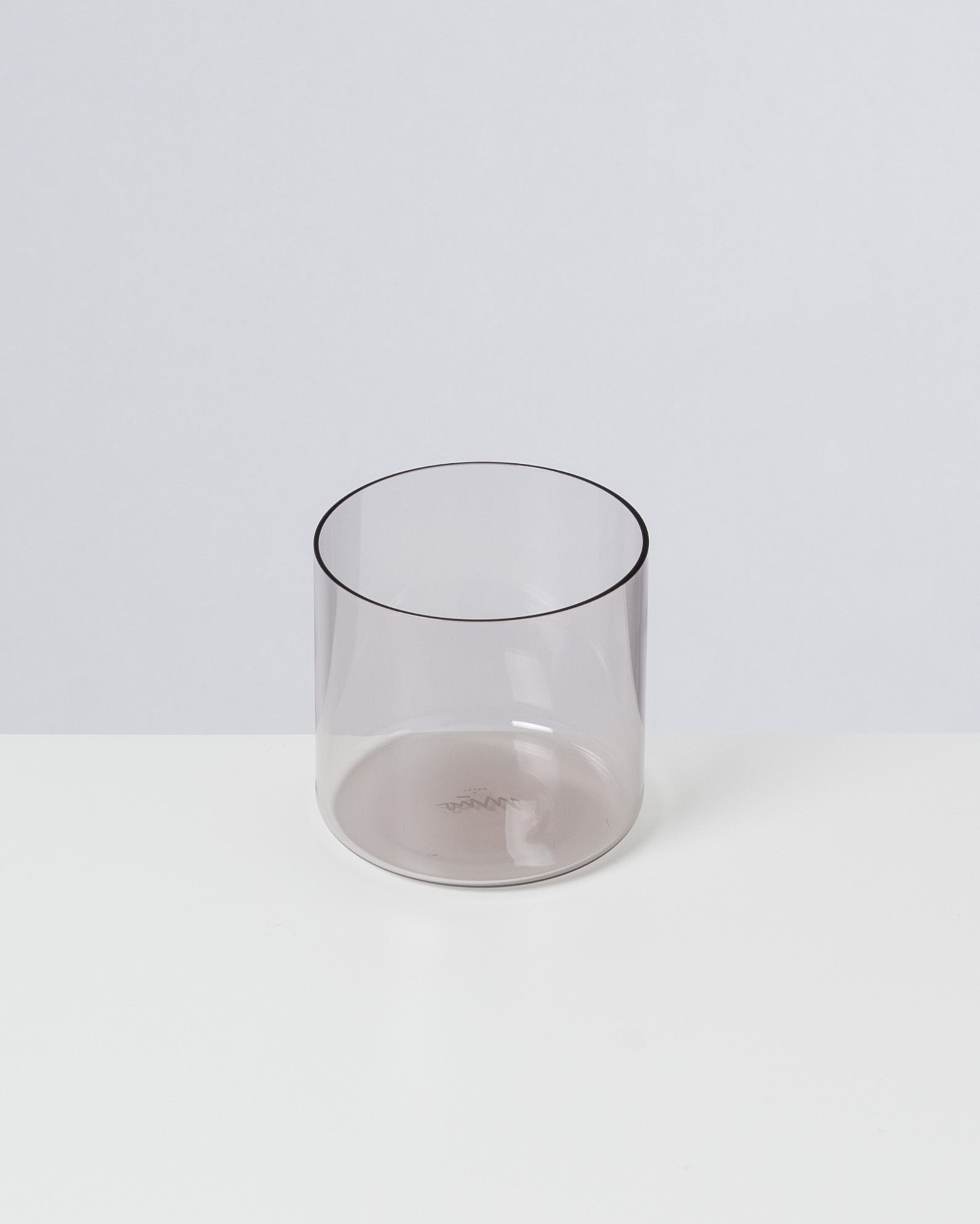Ein durchsichtiges, graues Glas steht auf einer weißen Oberfläche vor einem grauen Hintergrund.