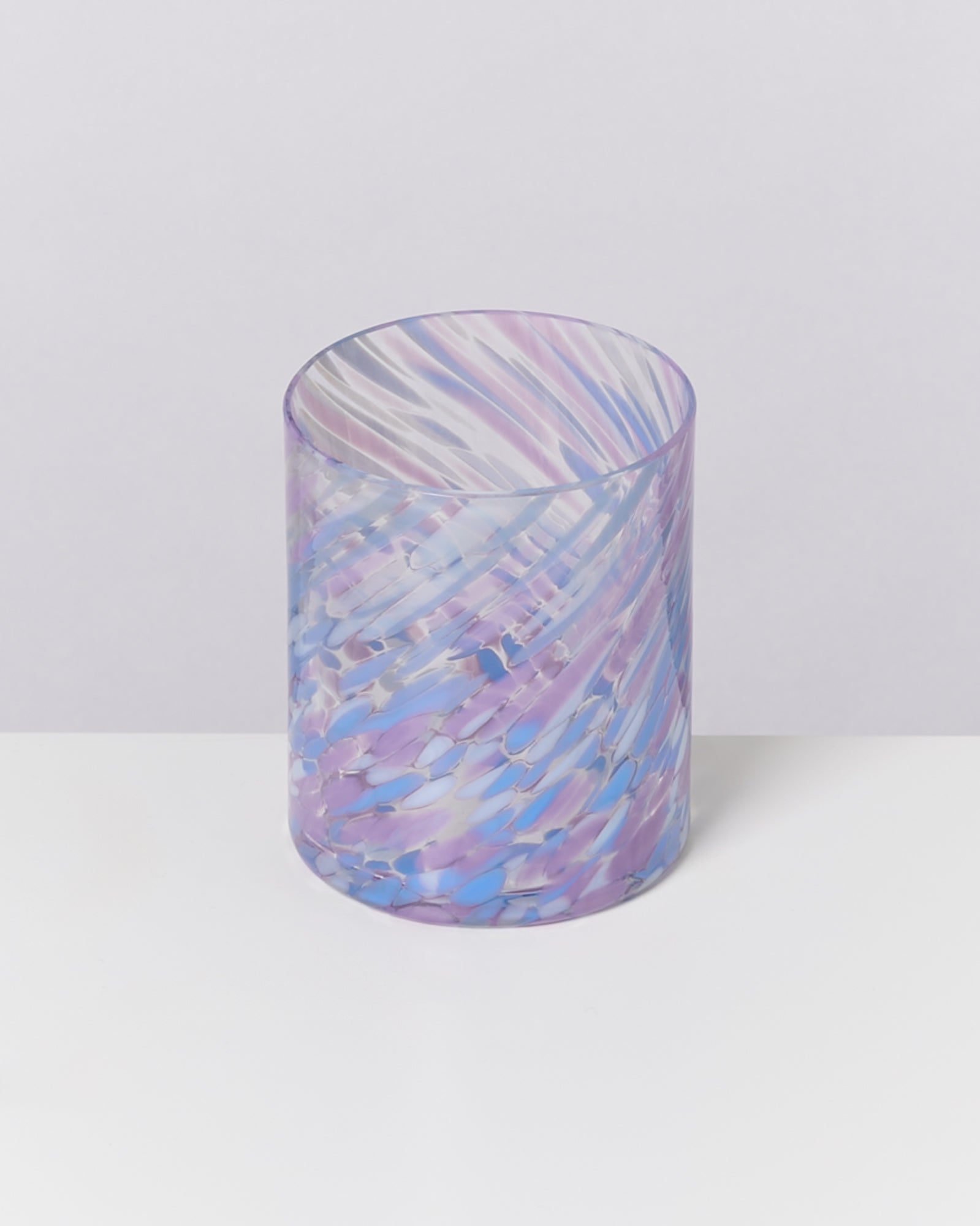 Ein zylindrisches Glas mit lila und blauen Wirbelmustern steht auf einem weißen Hintergrund.