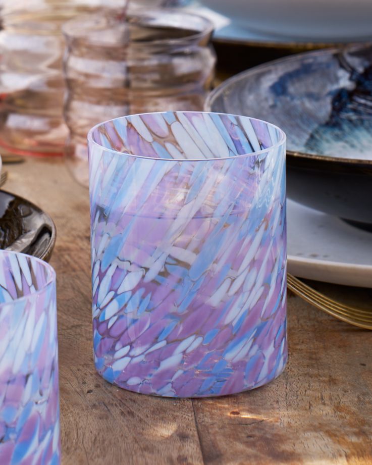 Ein Glas mit violettem und blauem Muster steht auf einem Holztisch neben Geschirr.