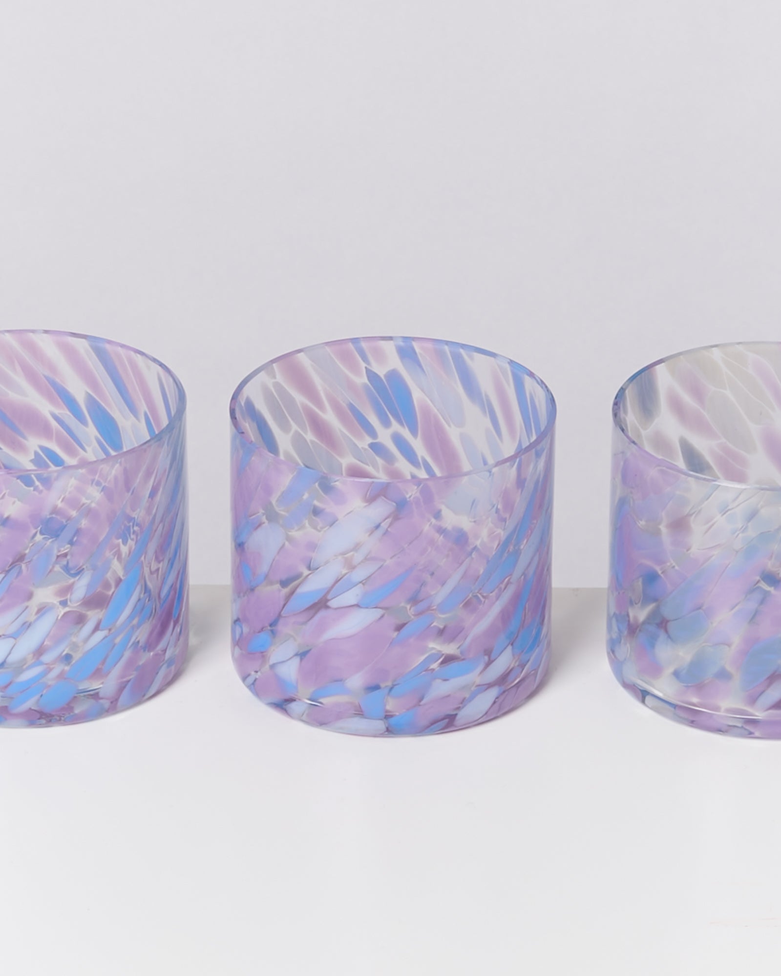 Drei bunte Gläser mit violetten und blauen Mustern auf weißem Hintergrund.