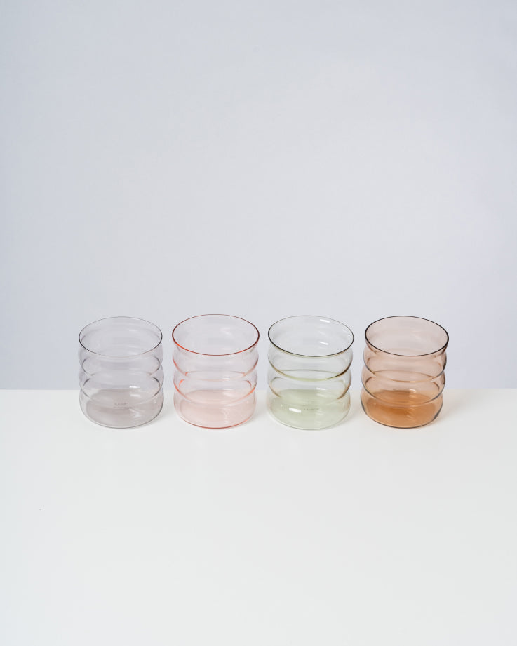 Vier farbige Gläser in einer Reihe auf einem weißen Tisch.