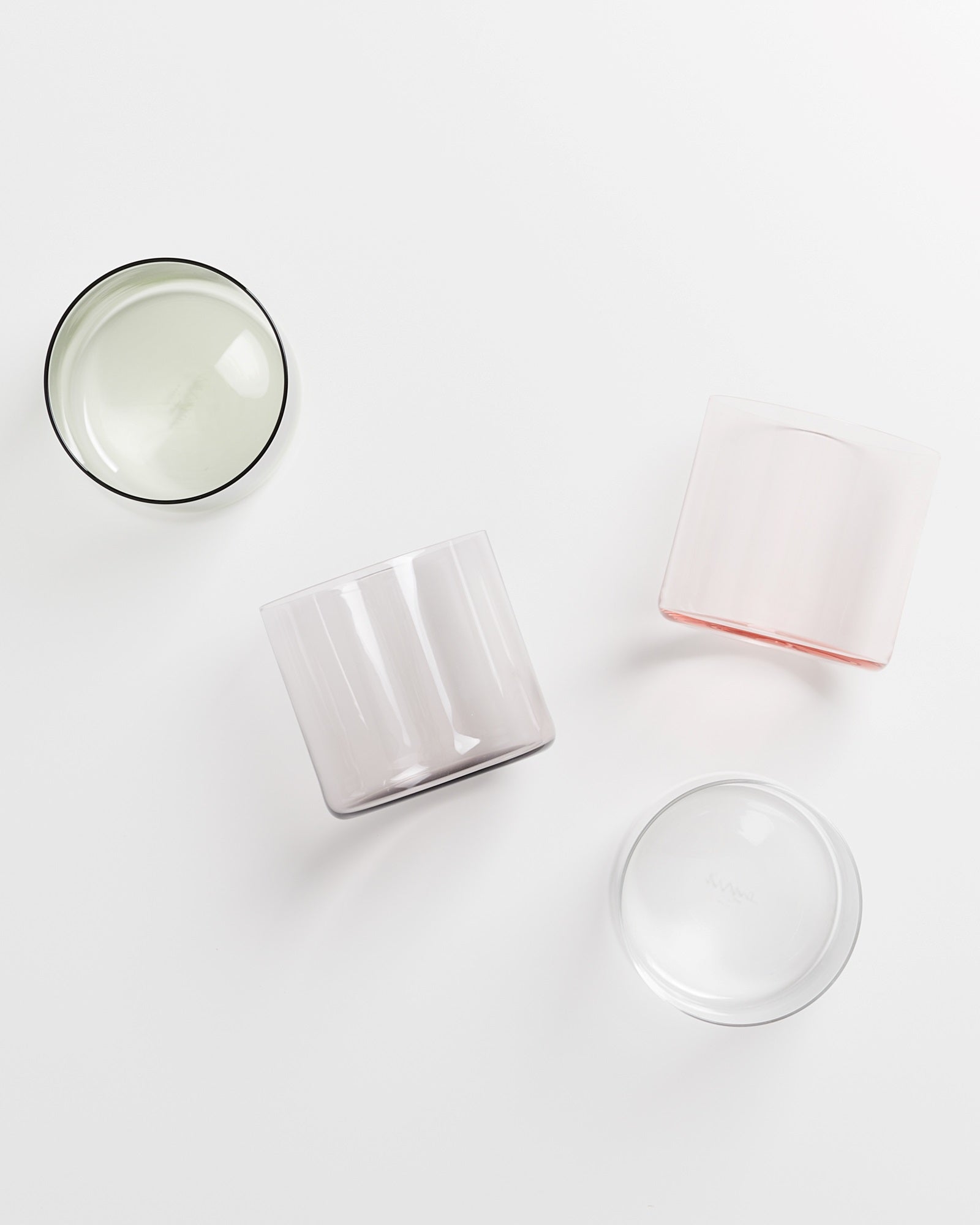 Vier farbige Glaskerzenhalter liegen auf einer weißen Oberfläche.