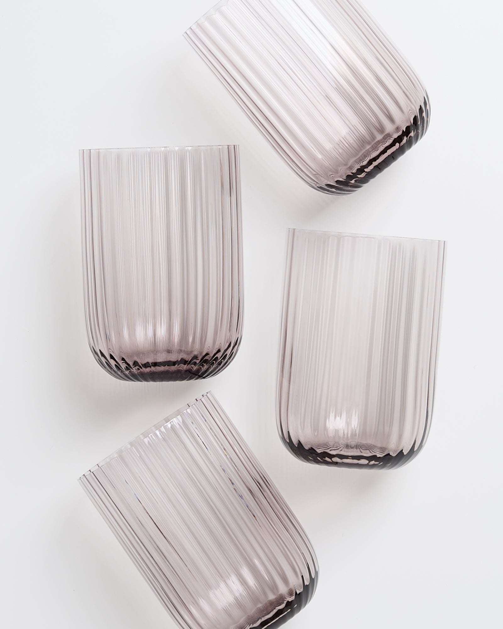 Vier geriffelte, leicht lilafarbene Gläser auf weißem Hintergrund.