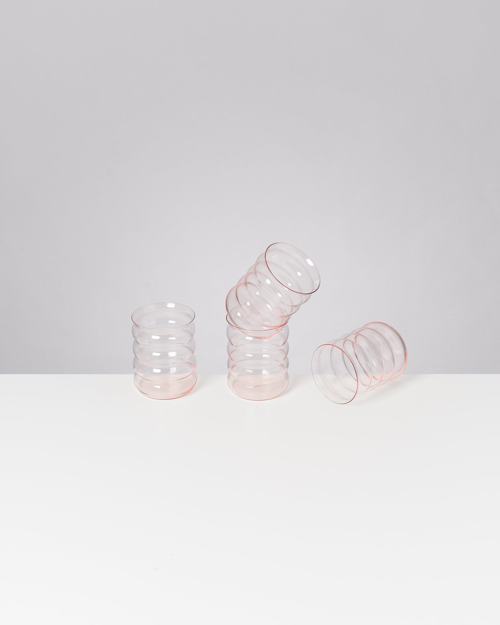 Drei gestapelte, rot umrandete Gläser auf weißem Tisch vor grauem Hintergrund.