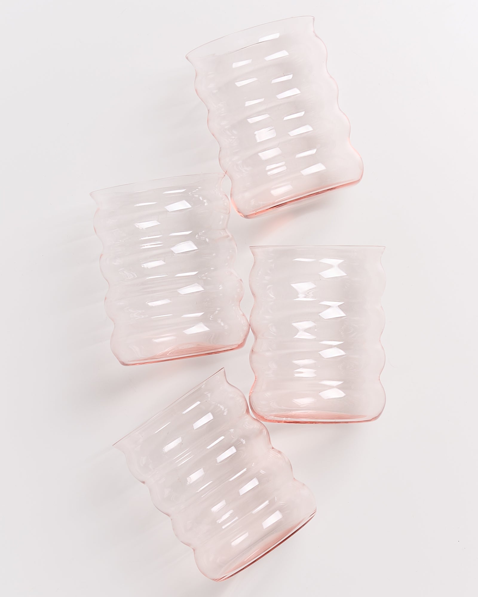 Vier rosa, gerillte Glasbecher liegen schräg nebeneinander auf weißem Hintergrund.