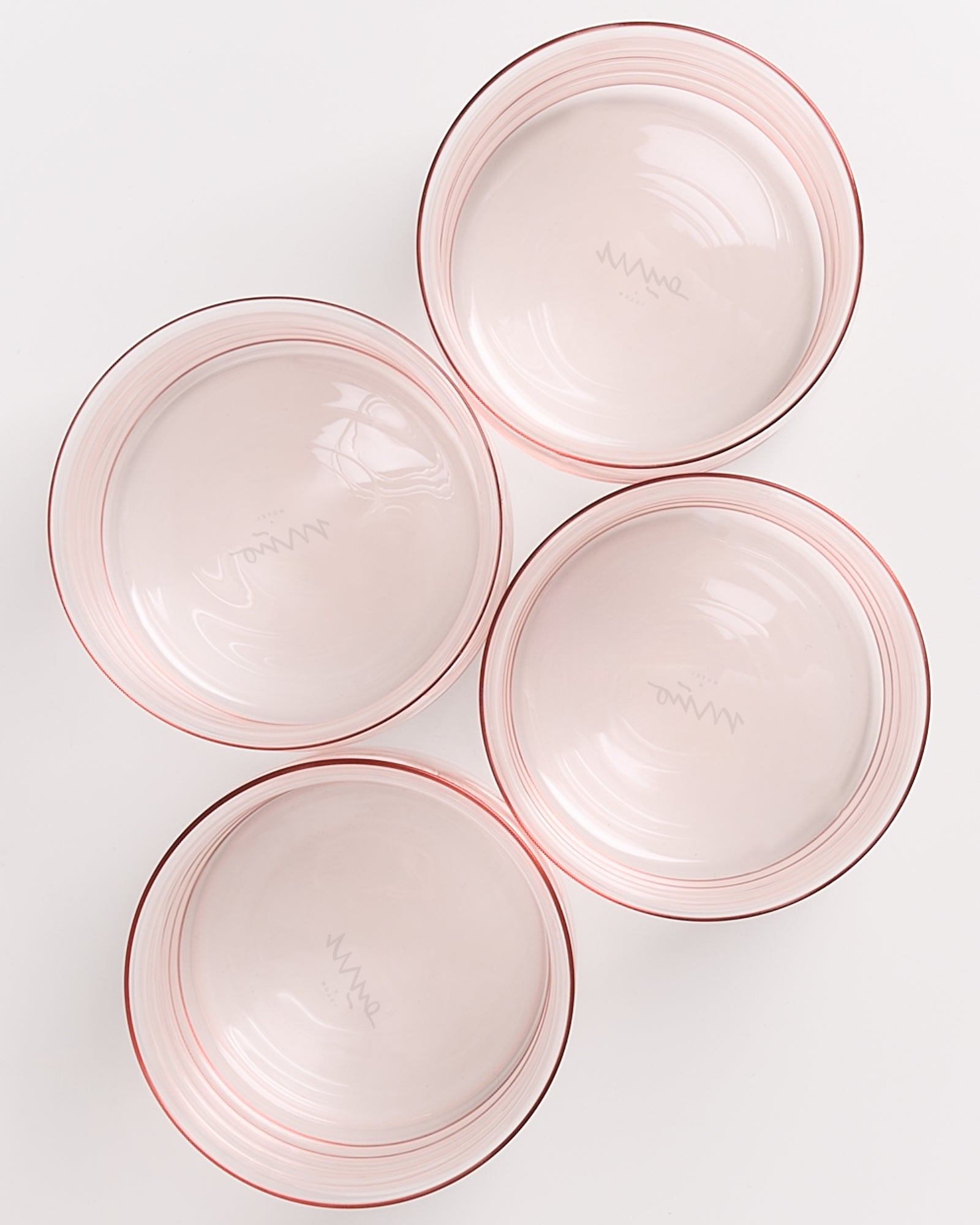 Vier rosa Glasschüsseln mit feinen Streifen, symmetrisch auf einer weißen Oberfläche angeordnet.