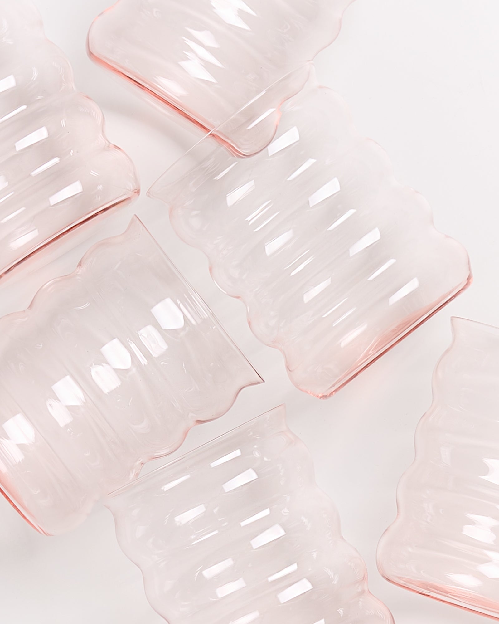 Wellenförmige, transparente rosa Gläser liegen diagonal auf einer weißen Oberfläche.