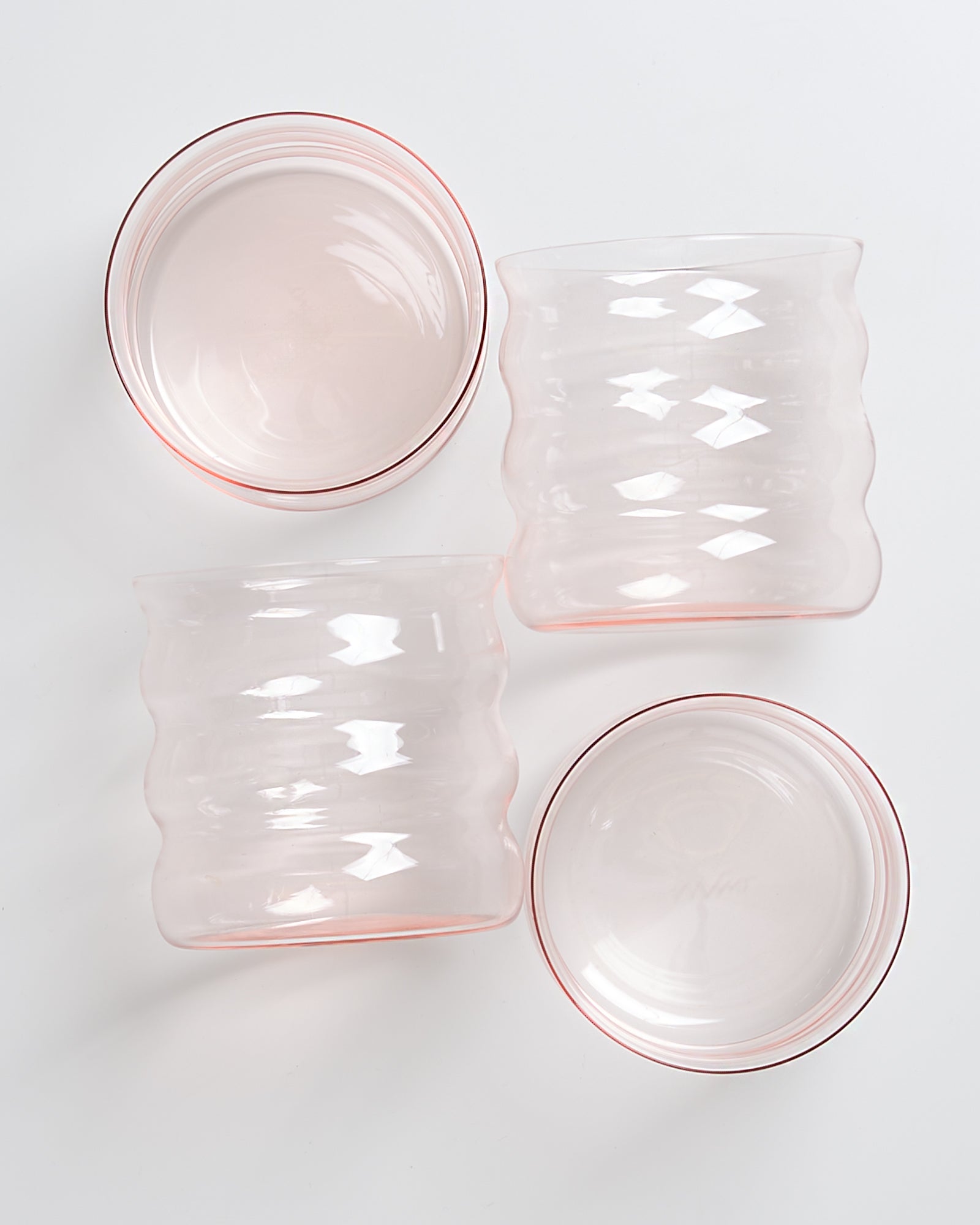 Vier rosa, gerippte Glasbecher liegen nebeneinander auf einem weißen Untergrund.