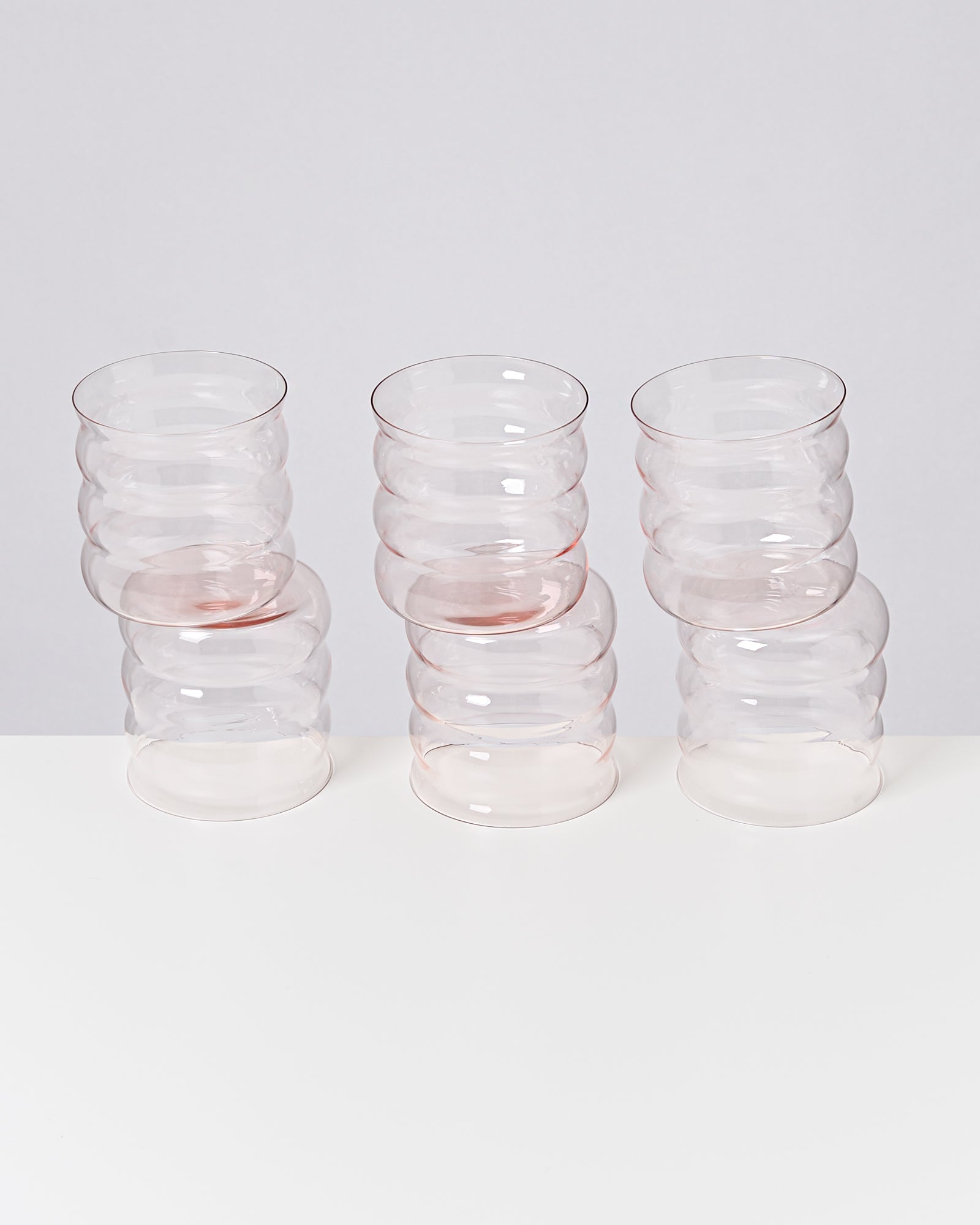 Sechs gestapelte, transparente Gläser mit gewelltem Design auf weißem Hintergrund.
