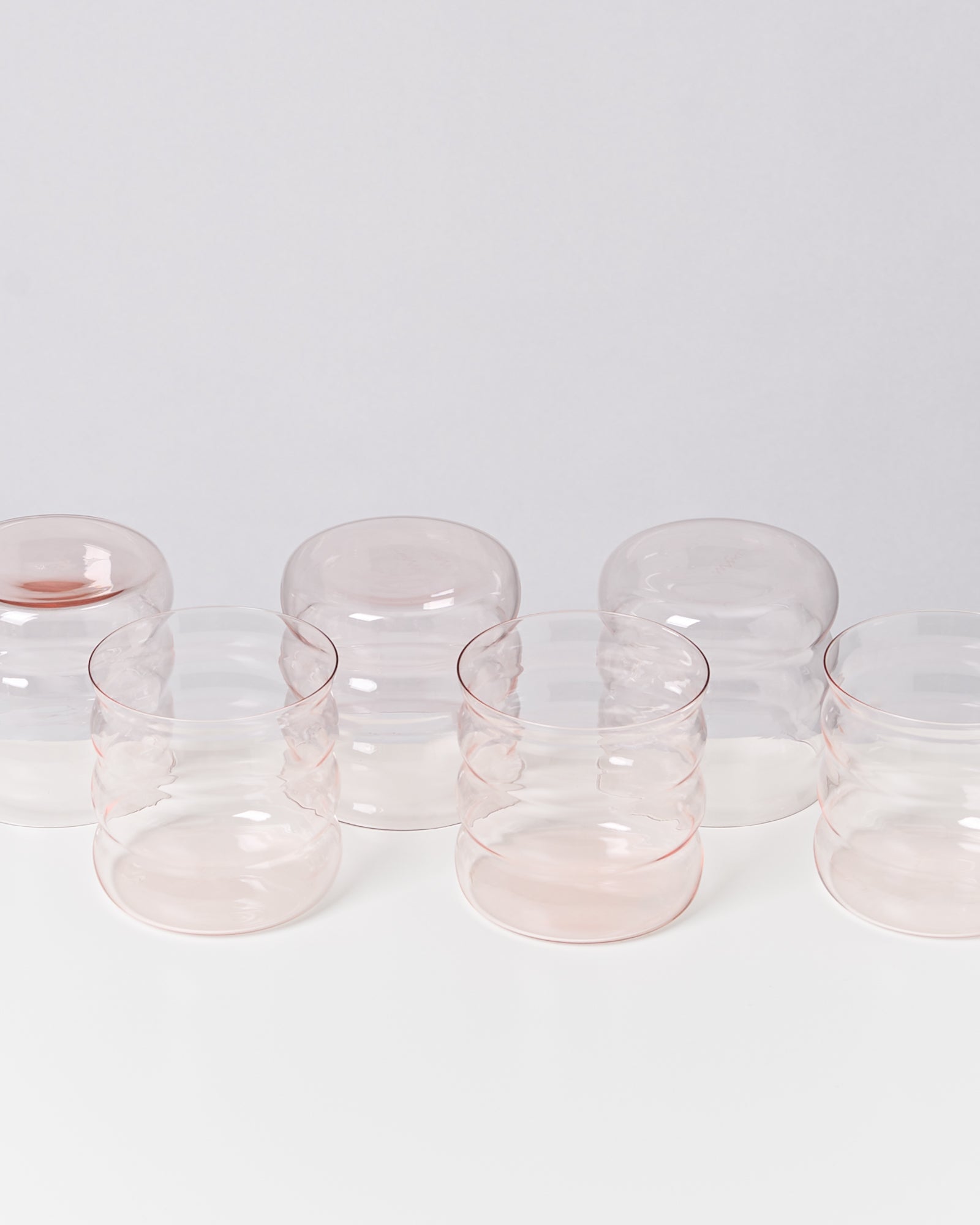 Fünf transparente, gewellte Gläser in Pastellrosa auf weißem Hintergrund.