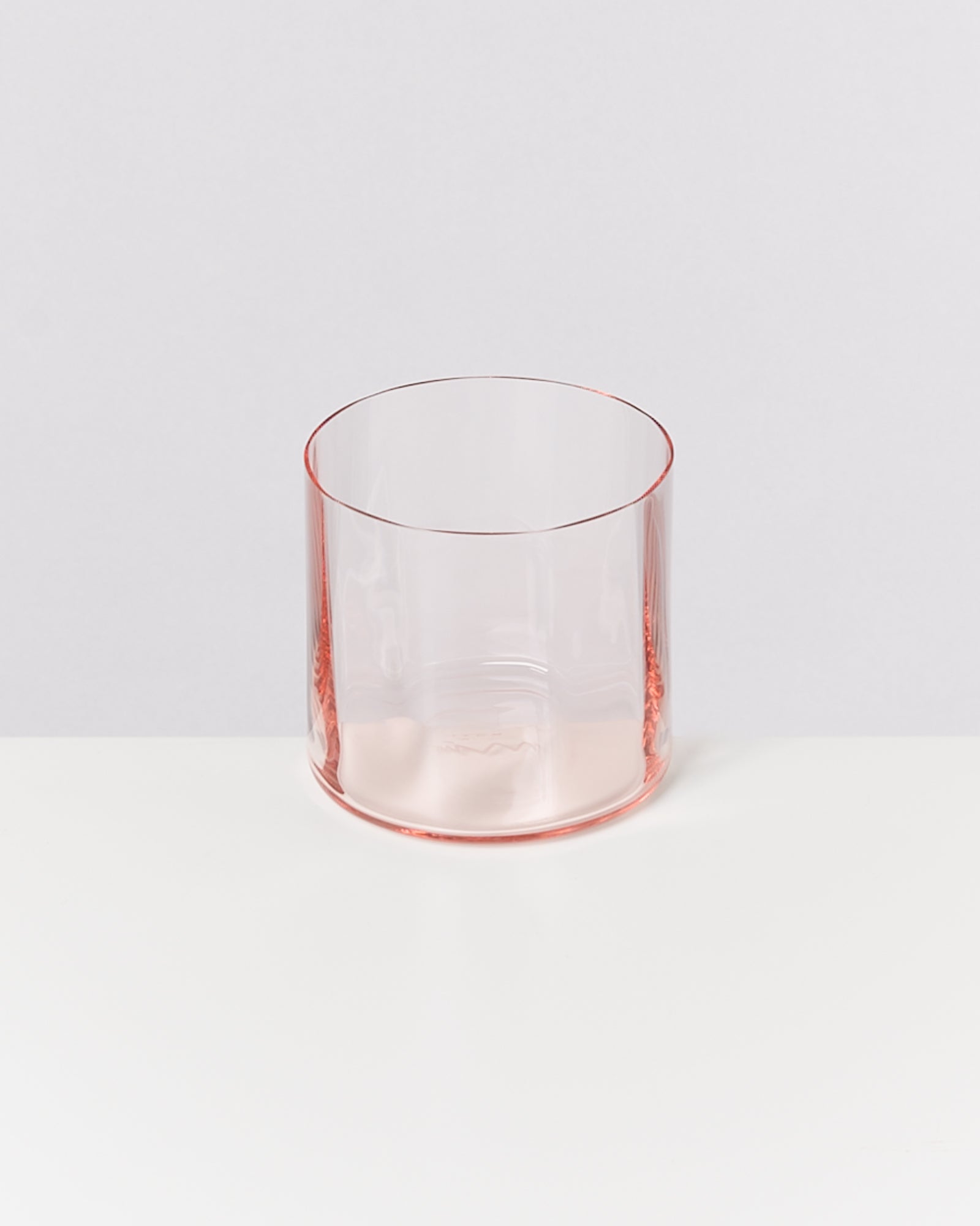 Ein transparenter, rosafarbener Becher steht auf einer weißen Oberfläche vor einem grauen Hintergrund.