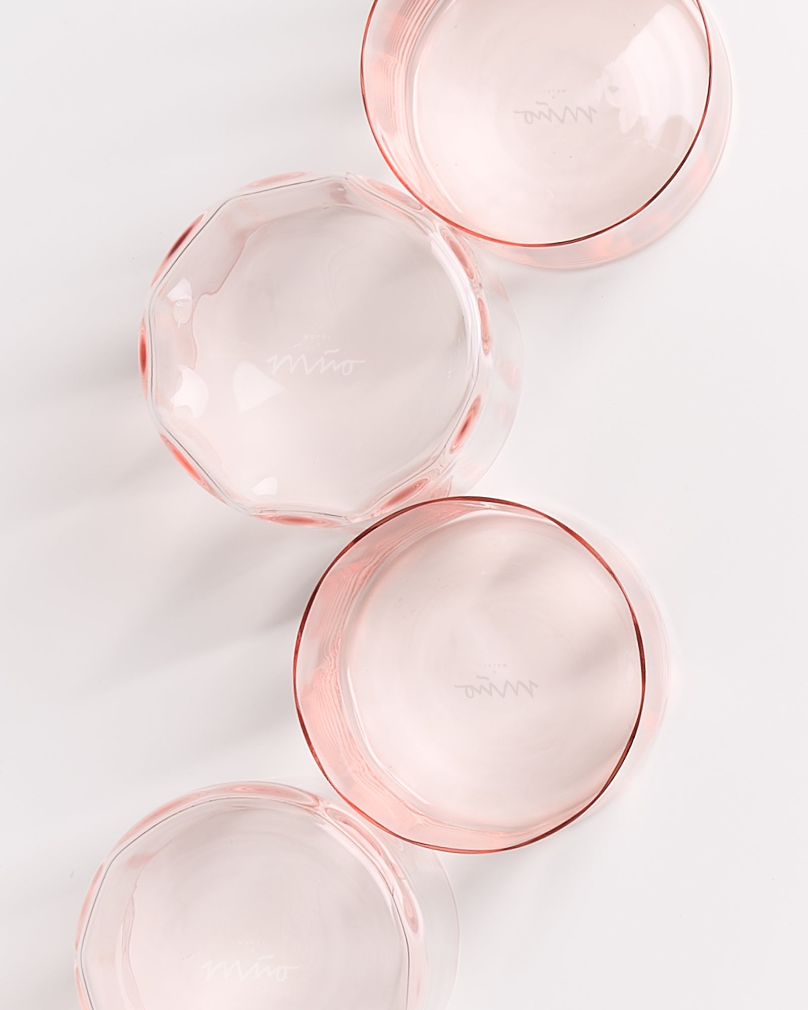 Vier rosafarbene Gläser mit rundem Design liegen auf einer weißen Oberfläche.