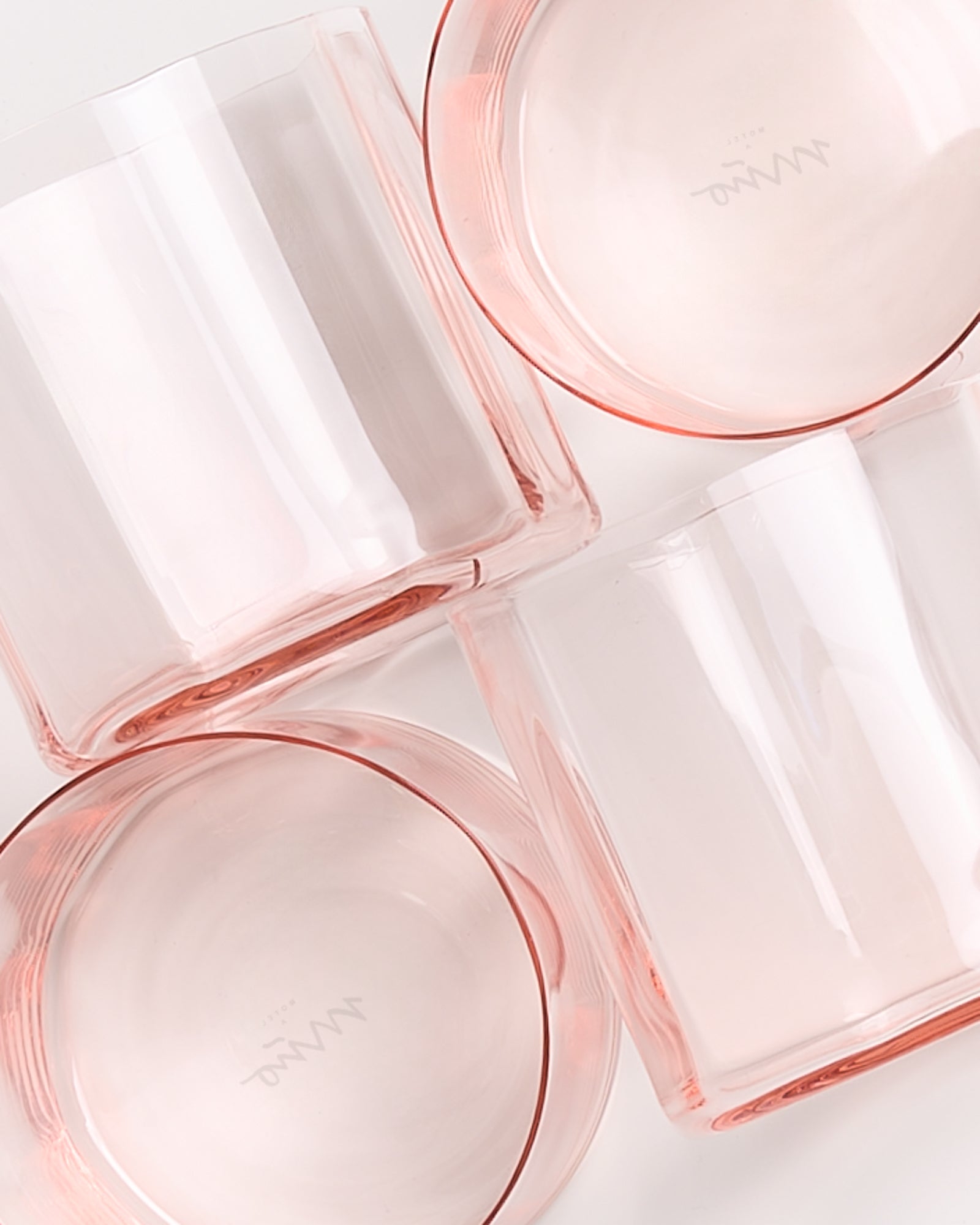 Vier rosafarbene Glasbecher liegen übereinander auf einer weißen Oberfläche.