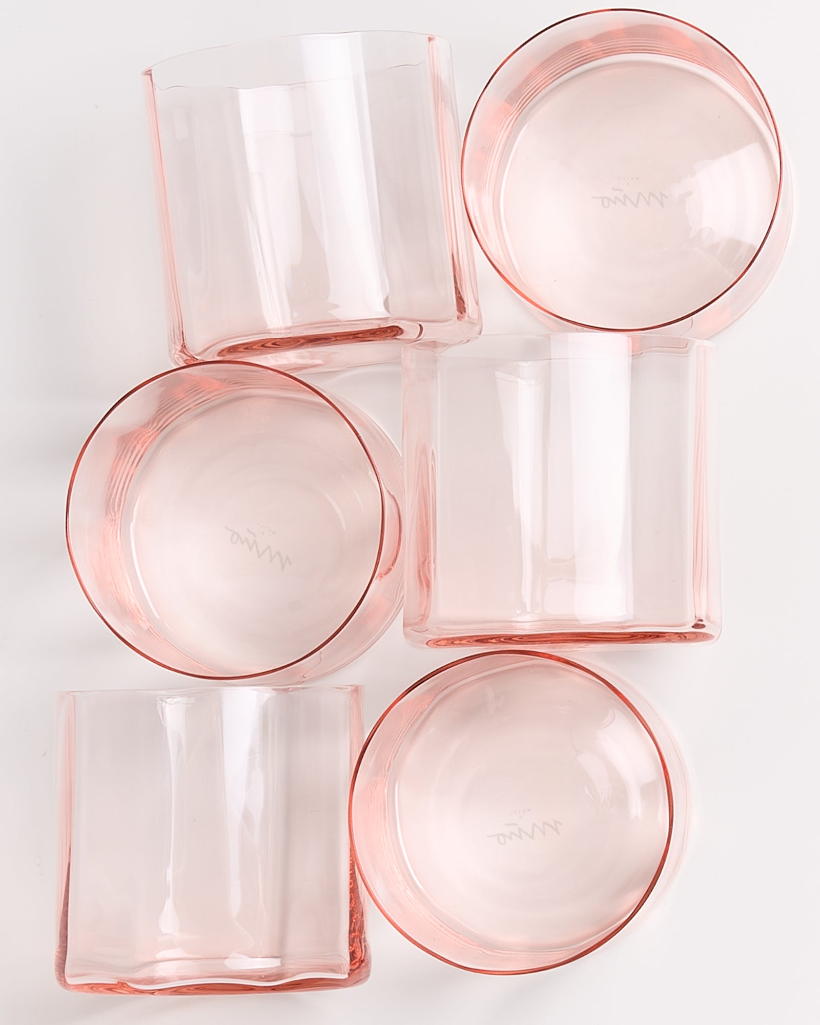 Sechs rosafarbene Gläser liegen in einer lockeren Anordnung auf einer weißen Oberfläche.