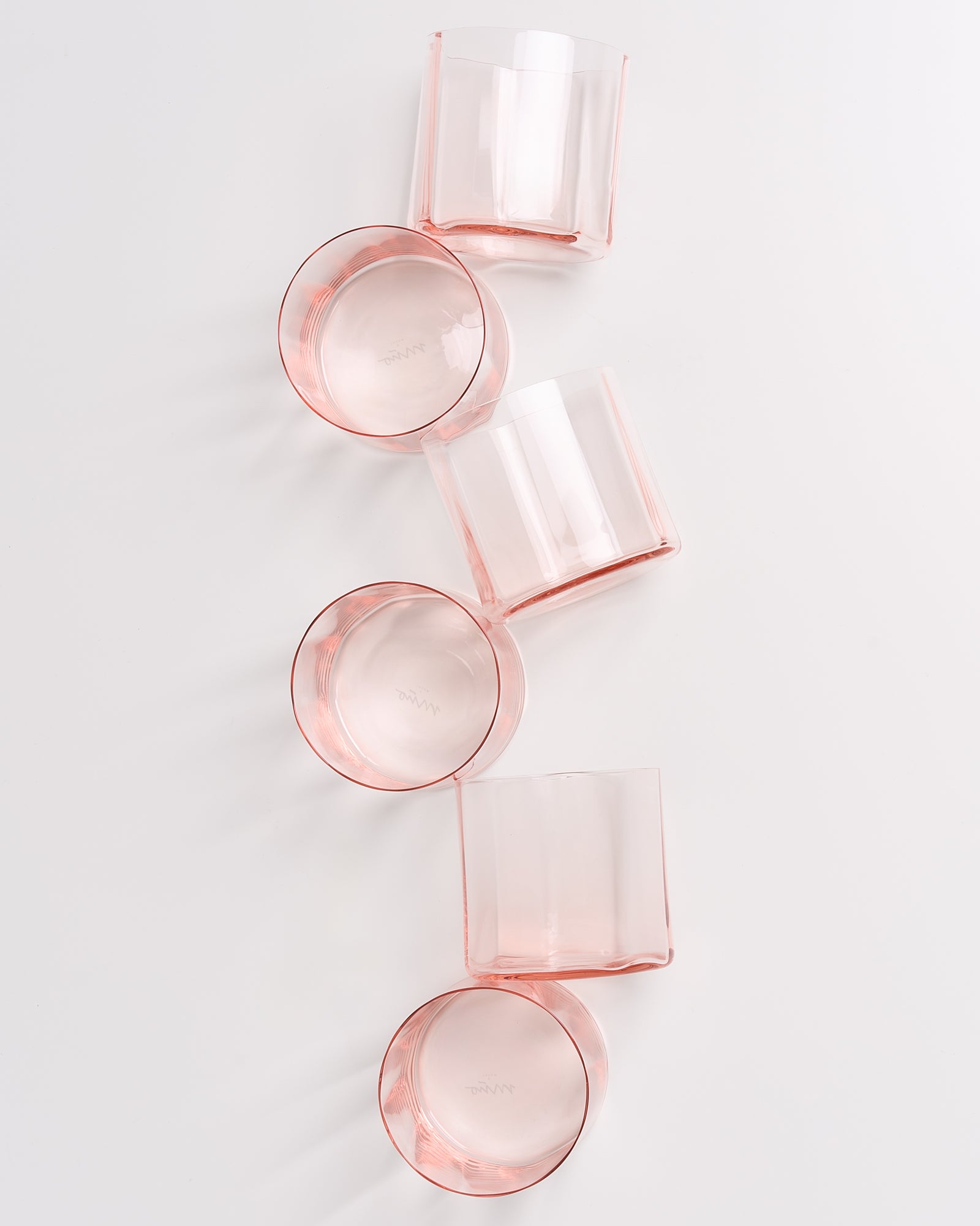 Fünf transparente, rosa Gläser liegen flach auf einer weißen Oberfläche in einer diagonalen Anordnung.