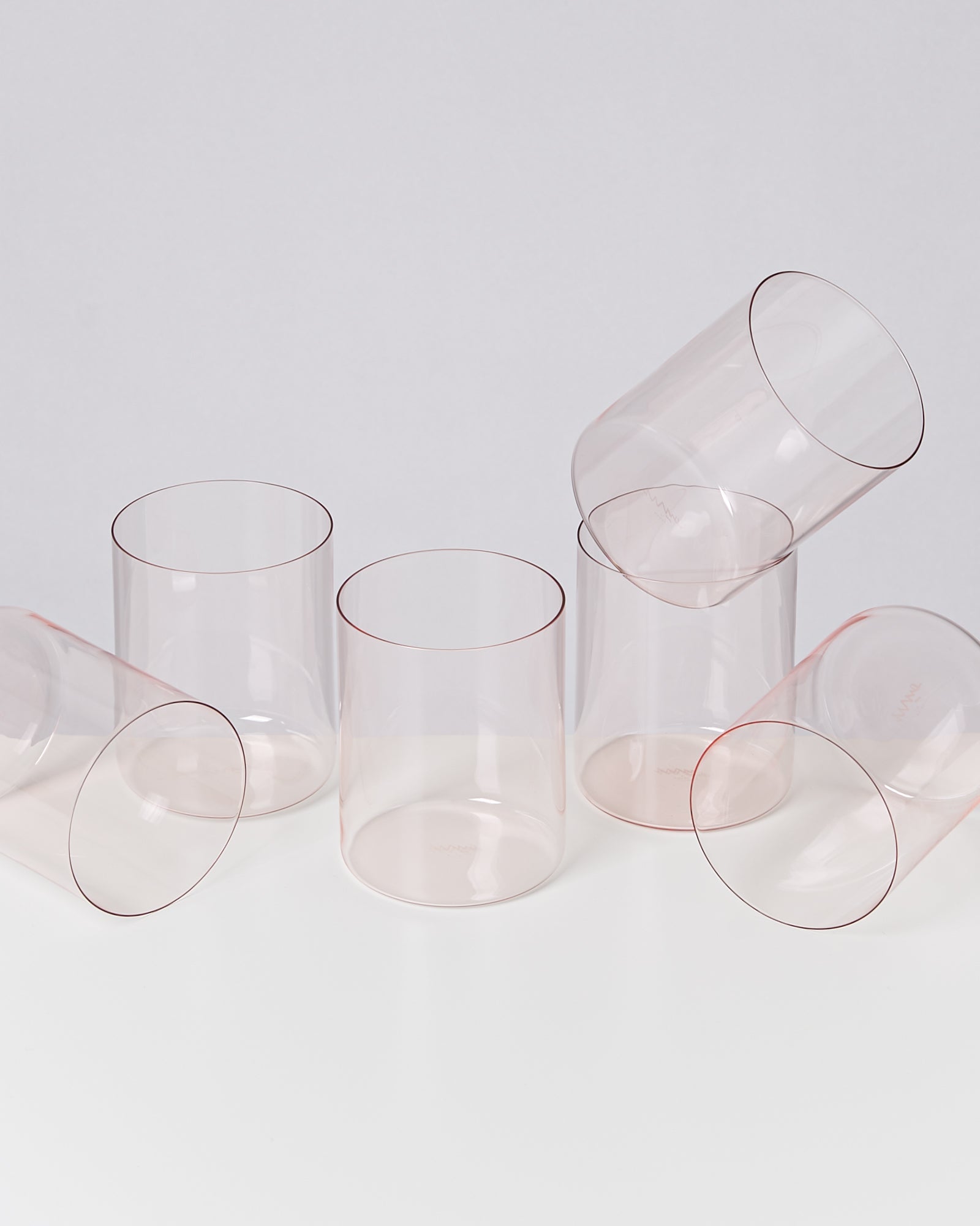 Sechs transparente Gläser, von denen einige aufrecht stehen und andere liegen auf einer weißen Oberfläche.