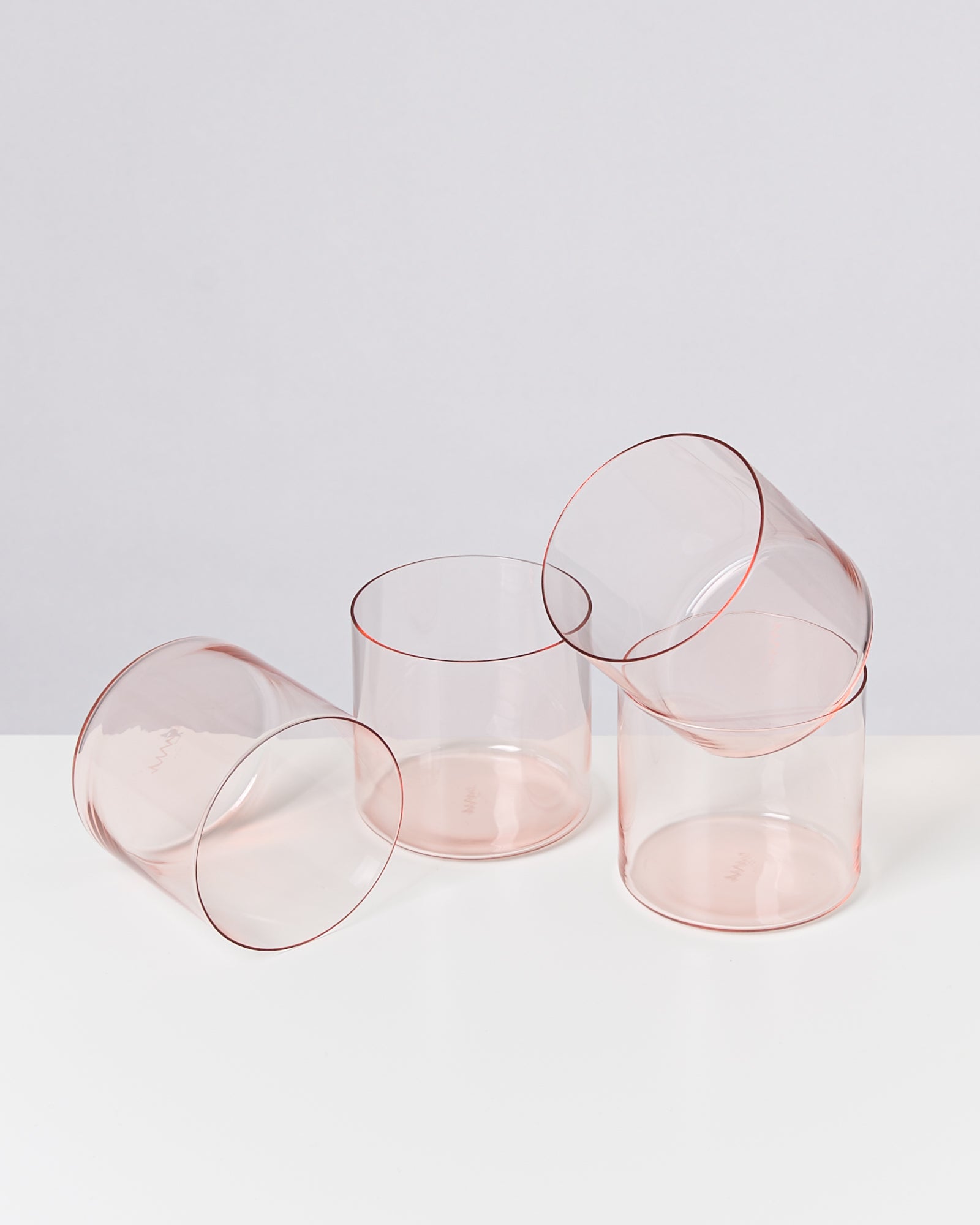 Vier transparente rosafarbene Gläser liegen auf einem weißen Untergrund.
