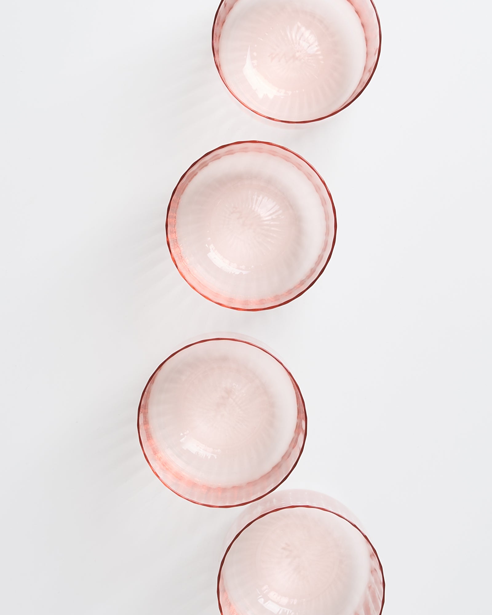 Vier rosafarbene Glasschalen mit rotem Rand sind in einer vertikalen Linie auf weißem Hintergrund angeordnet.