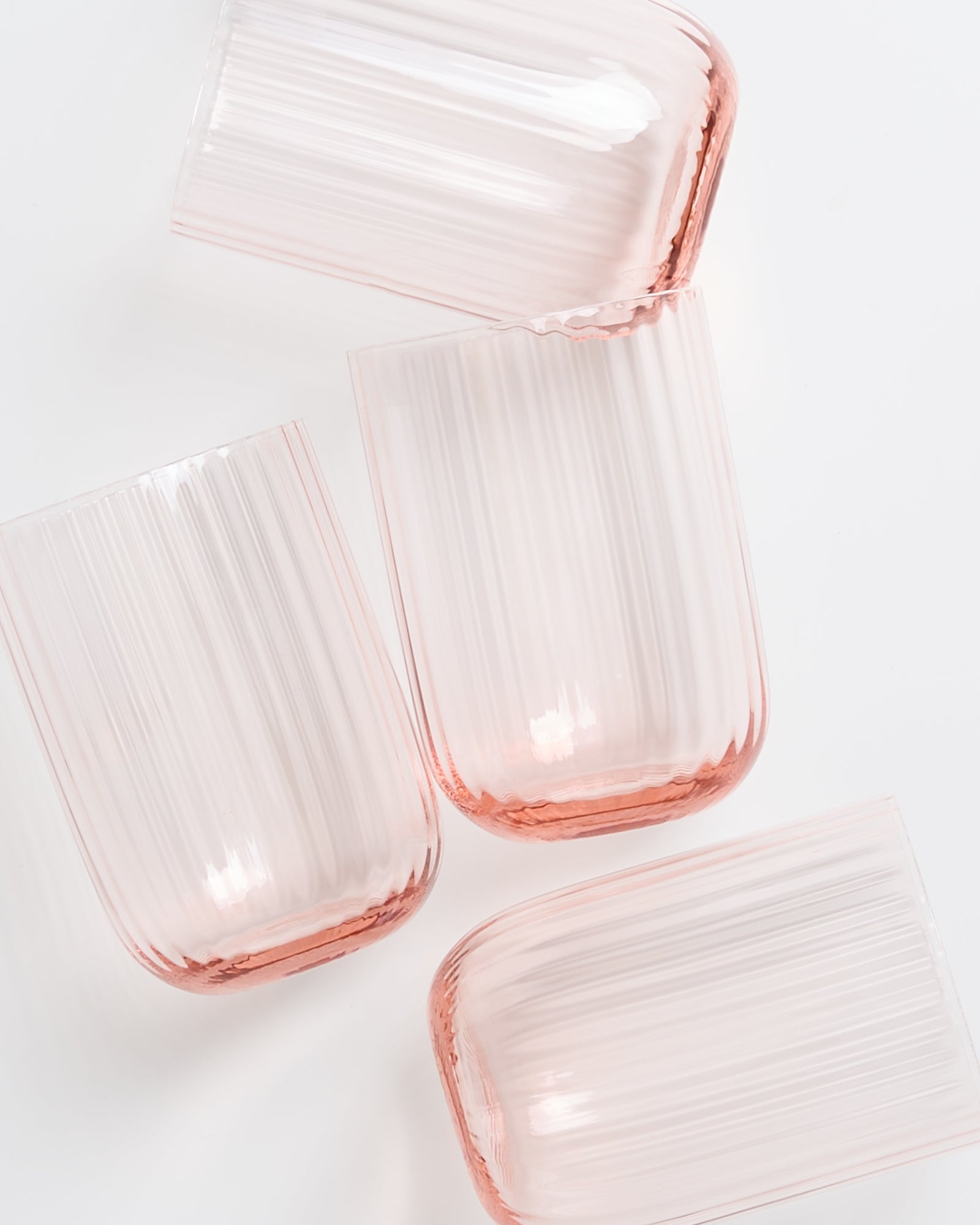 Vier rosafarbene, geriffelte Gläser liegen seitlich auf weißem Hintergrund.