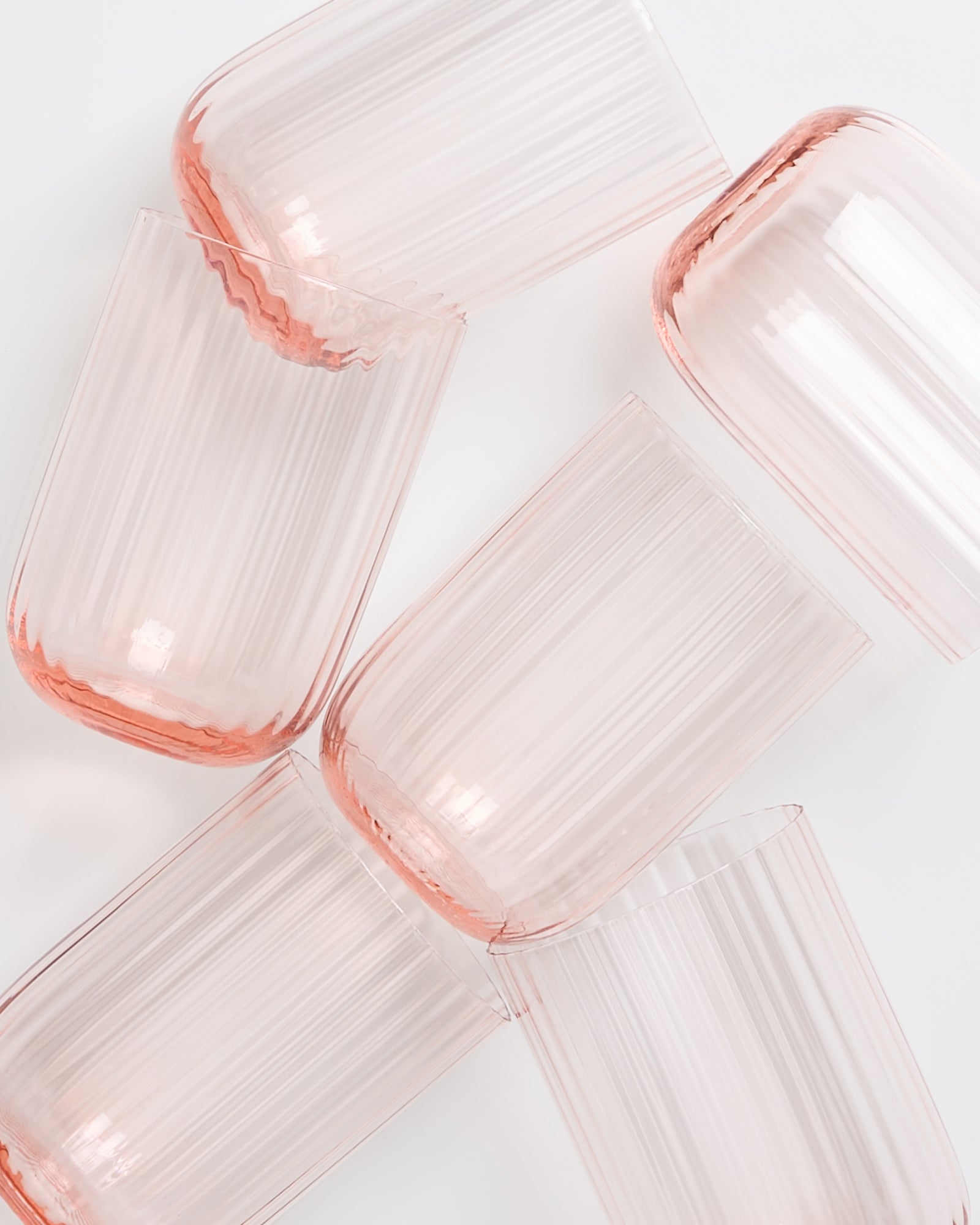 Sechs rosa, geriffelte Trinkgläser liegen zufällig auf einer weißen Oberfläche.