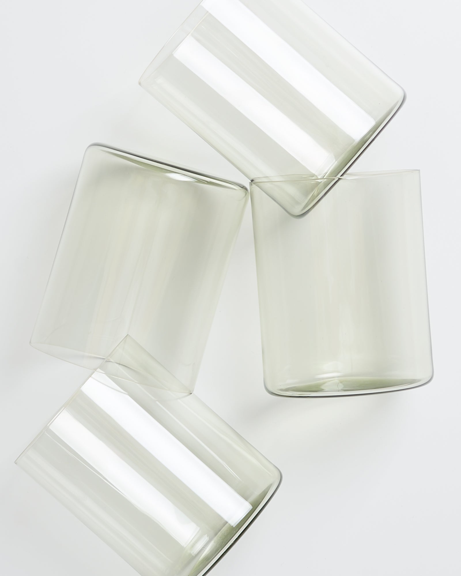 Vier transparente Gläser, die auf einem weißen Hintergrund schräg angeordnet sind.