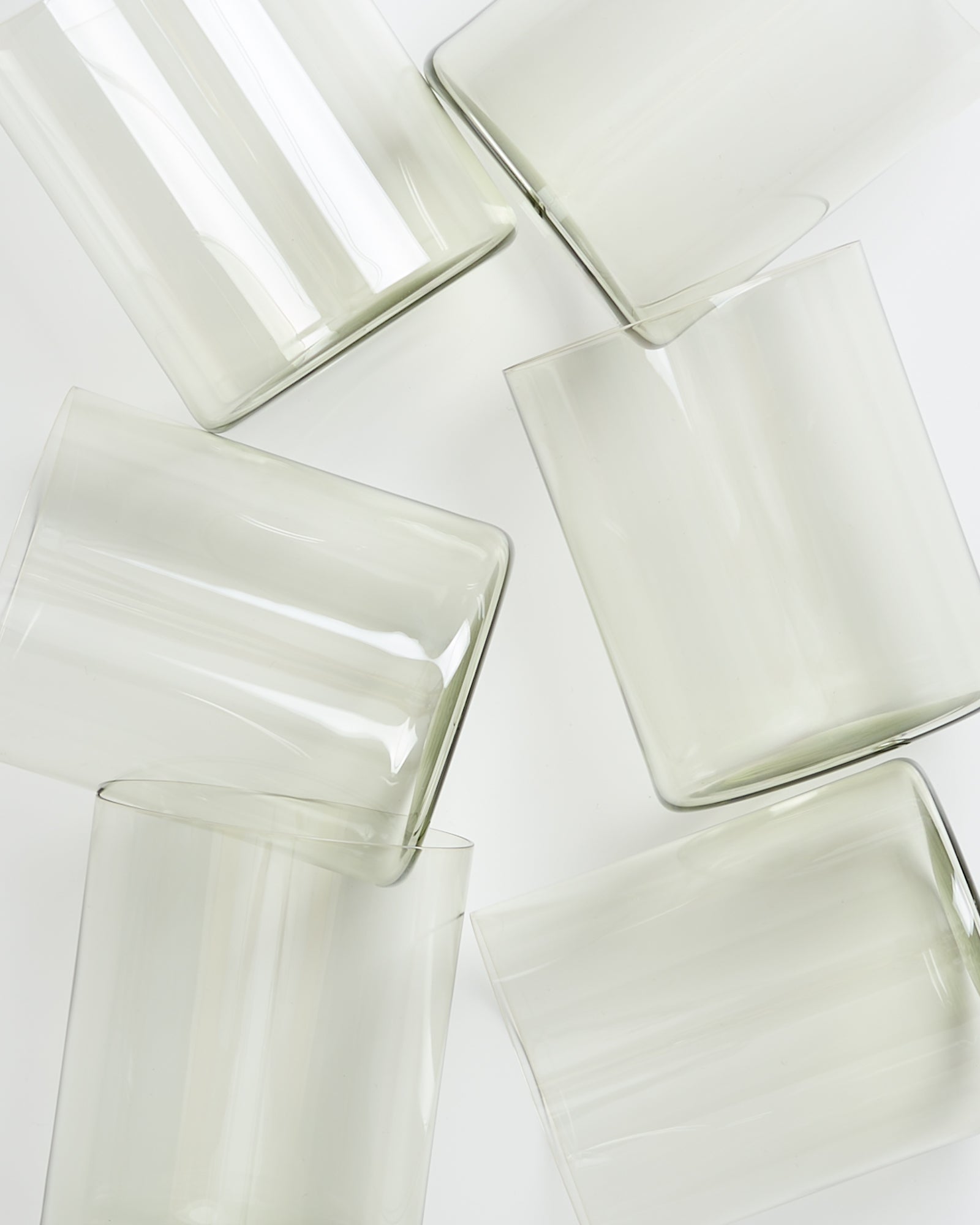 Sechs transparente, überlappende Glaszylinder liegen auf weißem Hintergrund verstreut.