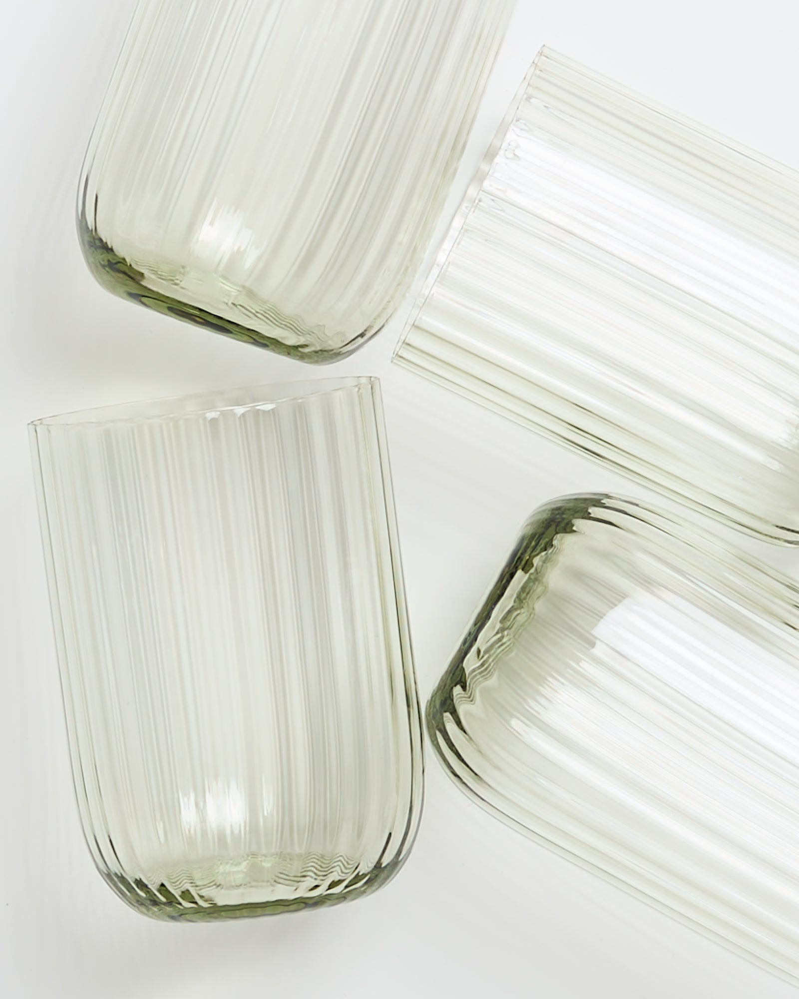 Vier geriffelte, durchsichtige Glasbecher liegen auf einer weißen Oberfläche.