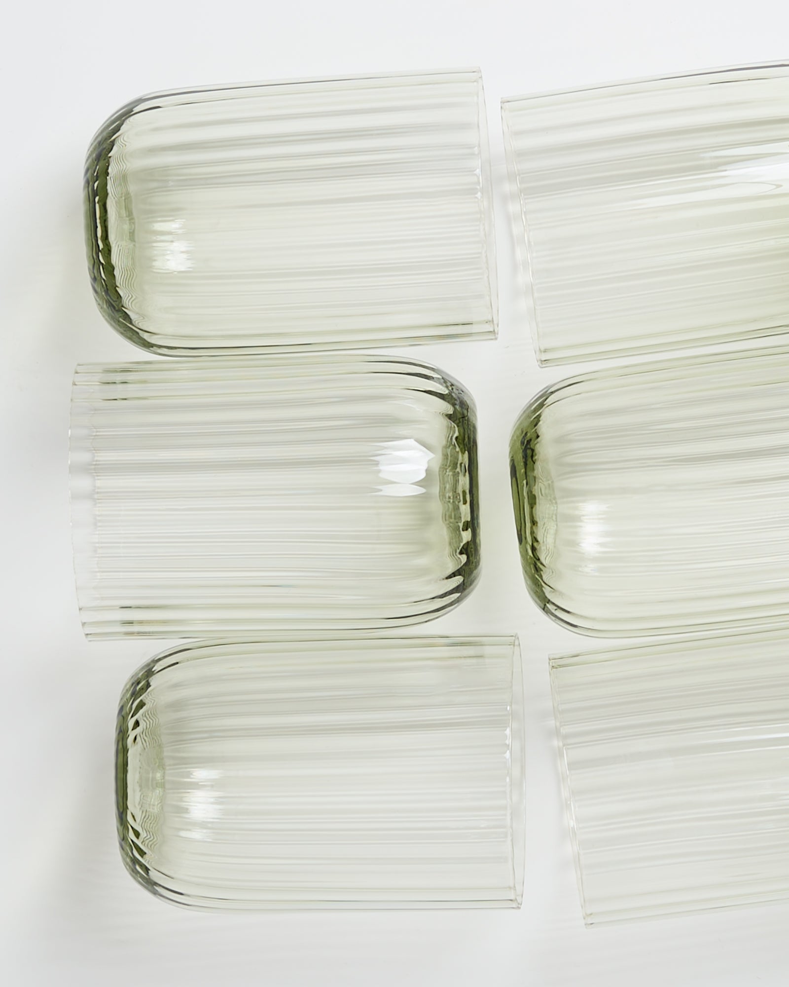 Sechs liegende durchsichtige Glasvasen mit geriffelter Oberfläche auf weißem Hintergrund.