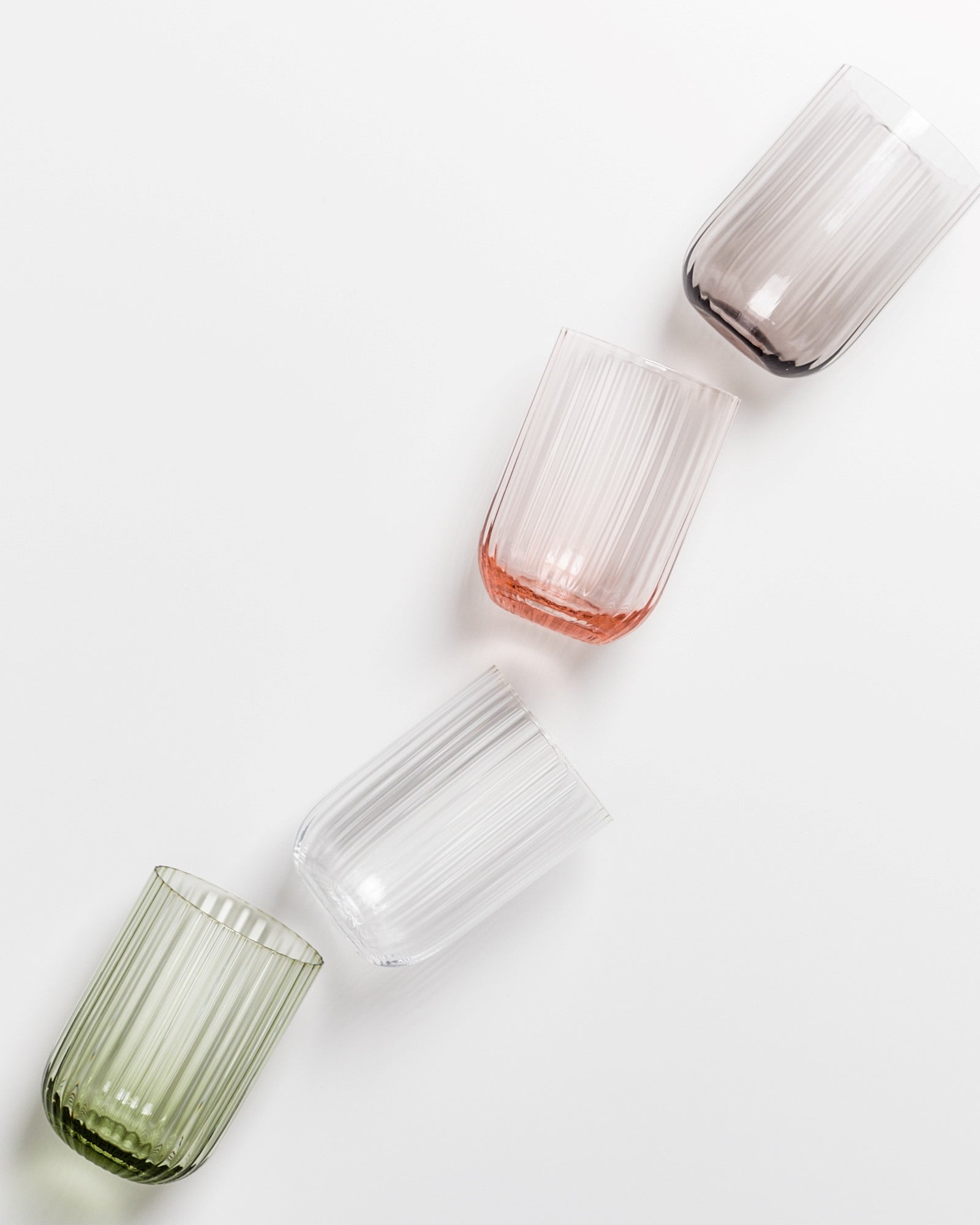 Vier gerippte Gläser in verschiedenen Farben liegen diagonal auf einer weißen Oberfläche.