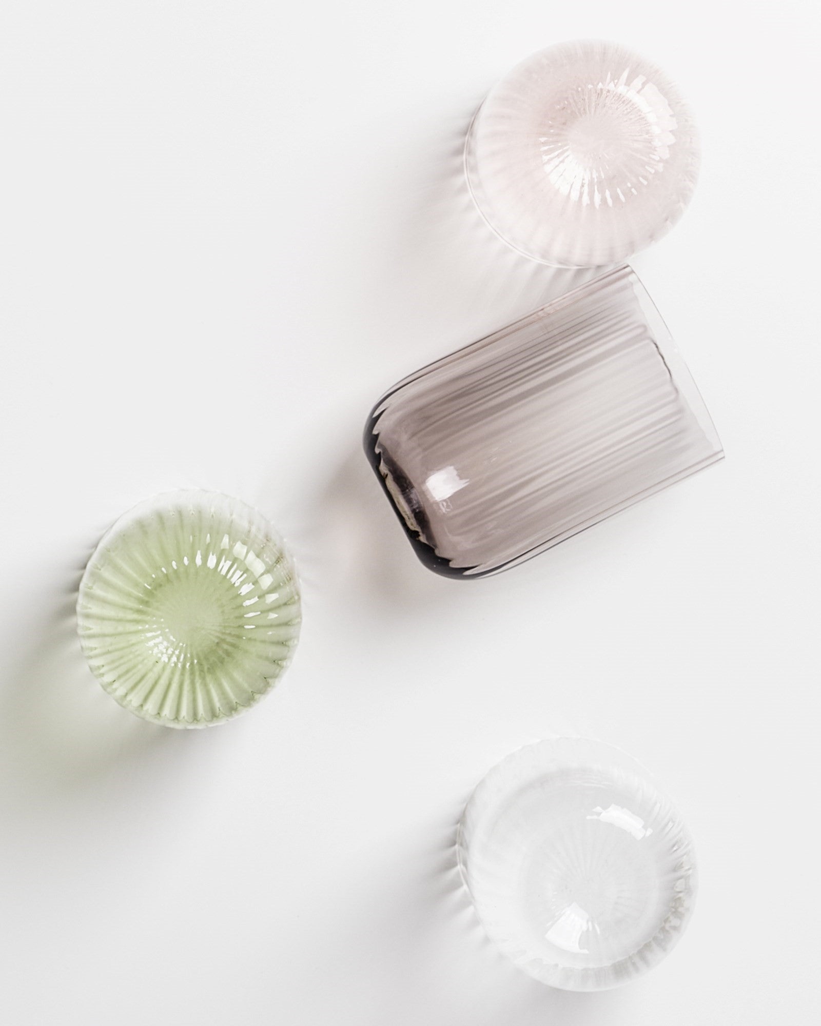 Vier durchsichtige Glasschalen in verschiedenen Farben und Formen liegen auf einer weißen Oberfläche.