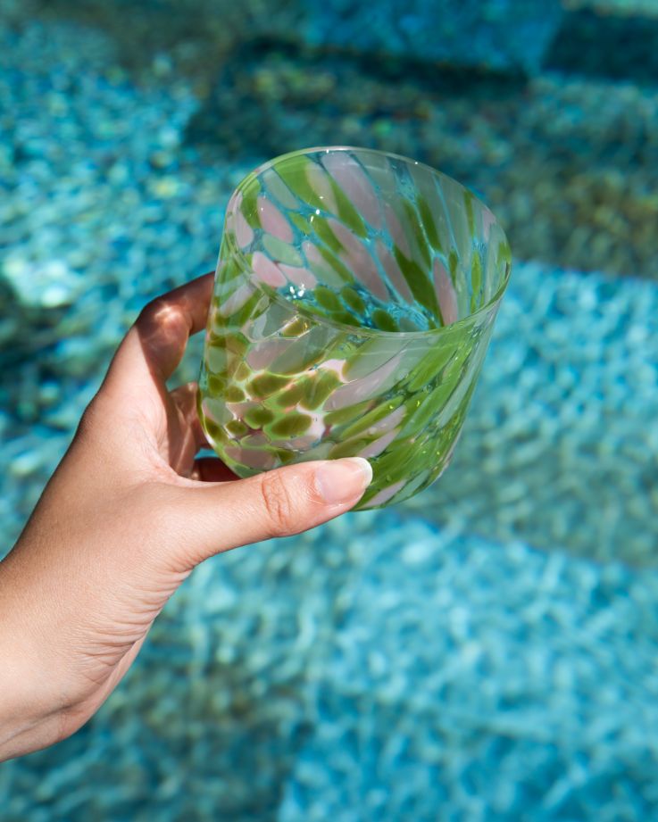 Hand hält ein grünes, gemustertes Glas über blauem Wasser.