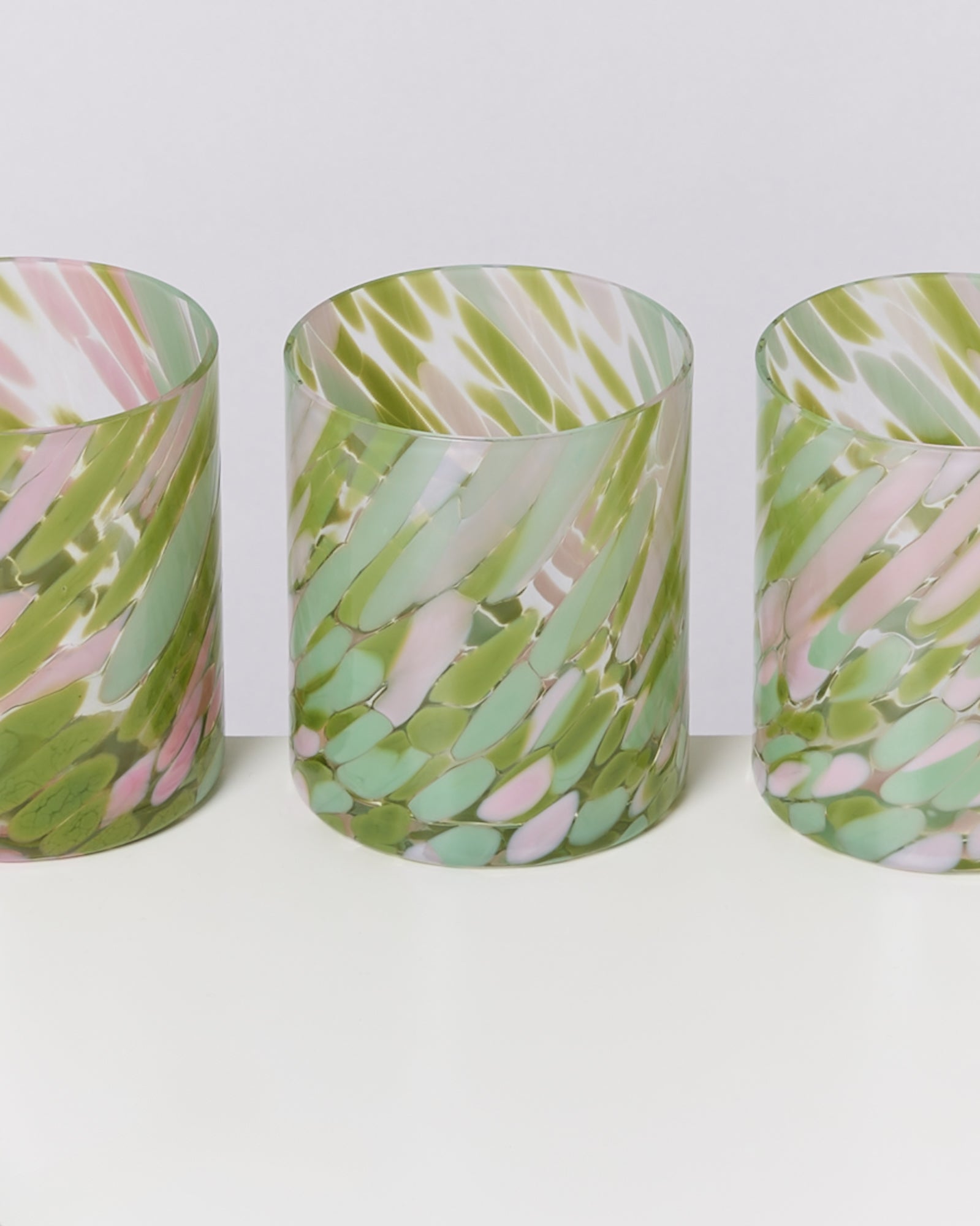 Drei bunte, glasierte Vasen mit grün-rosa marmoriertem Muster stehen auf einer weißen Oberfläche.